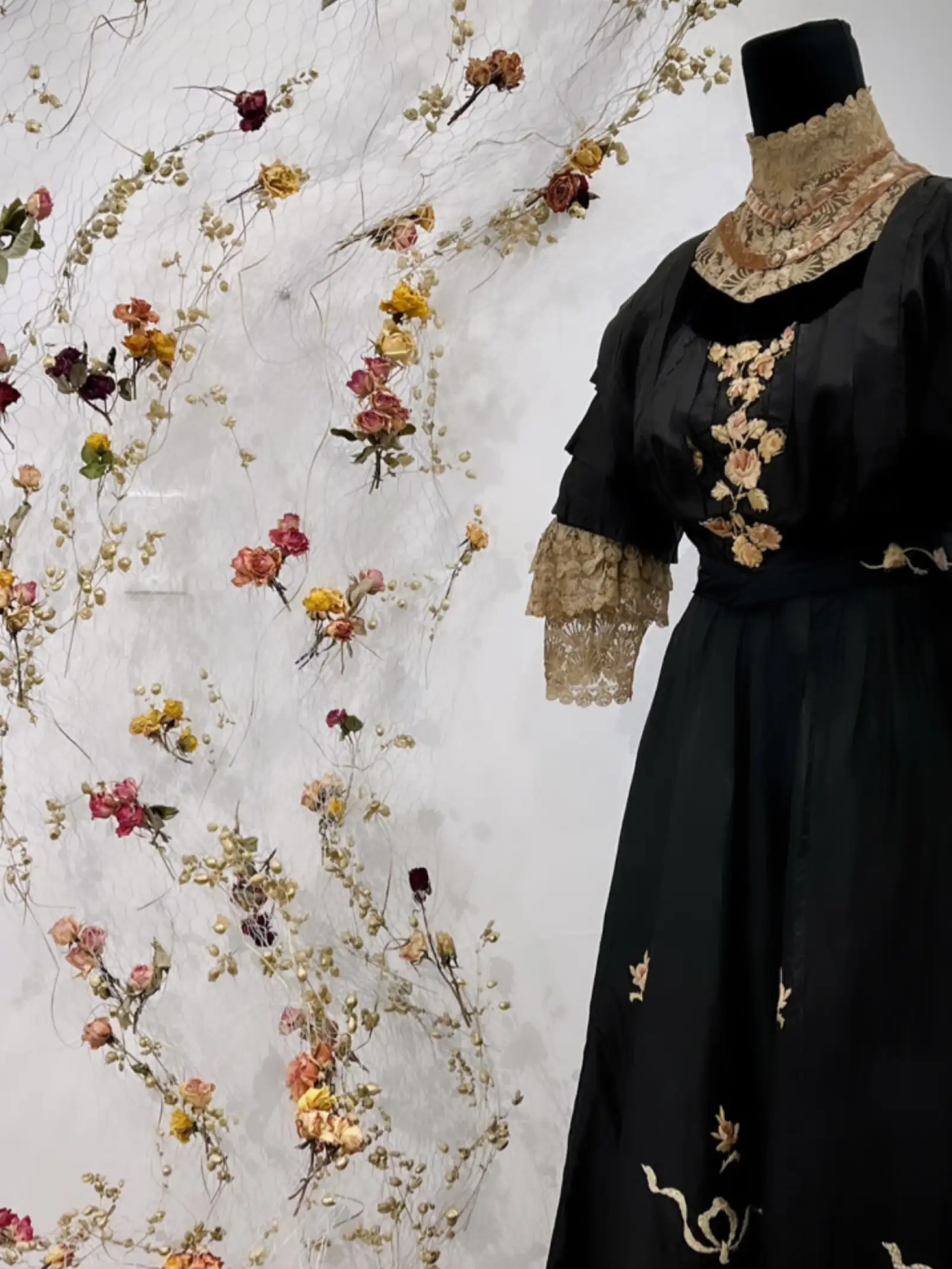 Instalación floral con vestido negro bordado para exposición de moda que combina arte textil y naturaleza preservada.