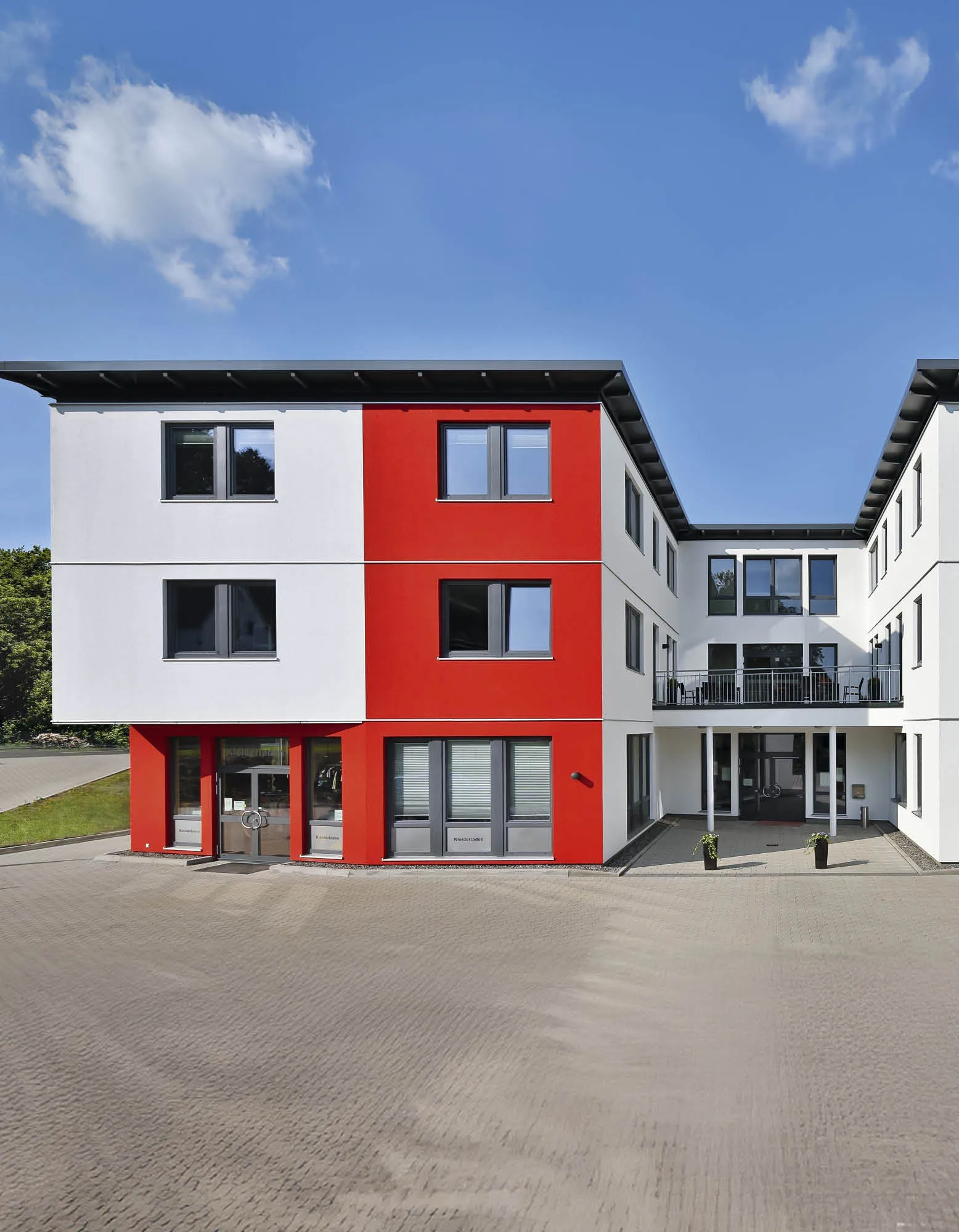 Modernes Gebäude mit roter und weißer Fassade, Fenster und Balkonen vor blauem Himmel.