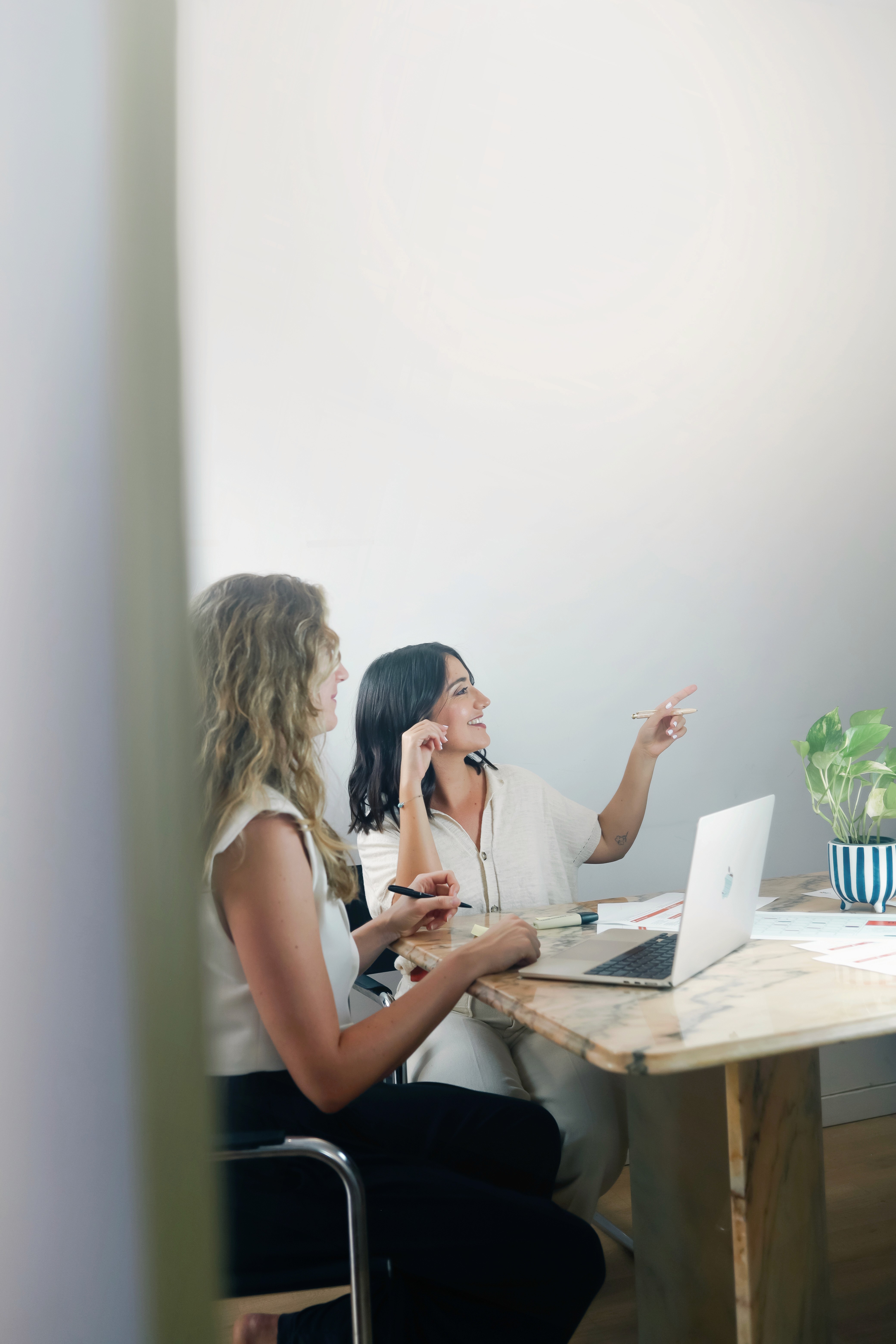 Two colleagues collaborating at a desk, reviewing project materials and pointing at a laptop during a strategy session