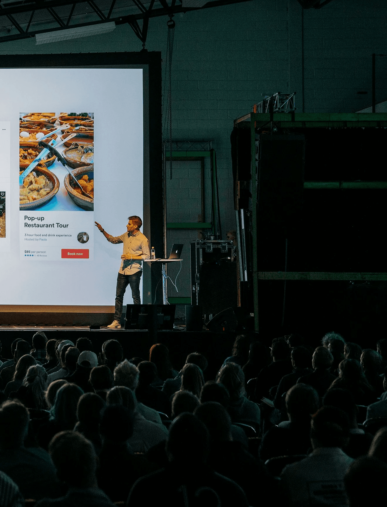 person discussing while standing in front of a large screen in front of people inside dim-lighted room