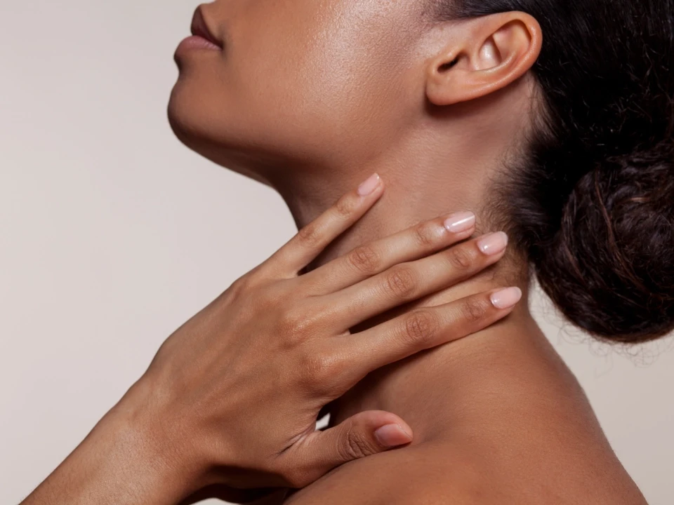 A woman lying down in a spa setting, relaxing with her eyes closed. Sunlight streams through blinds, casting striped shadows on her face. The scene conveys a sense of serenity and well-being.