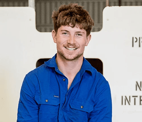 Close-up portrait of a freckled woman with soft pink hair and star earring, natural light, white tank top.