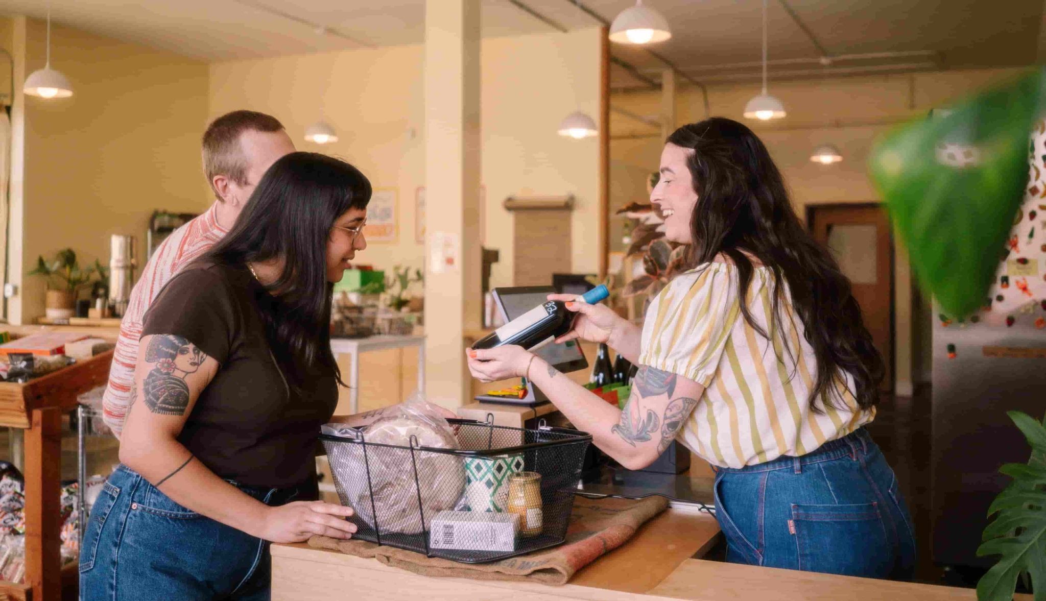 Cliente observa garrafa de vinho segurada por atendente atrás de balcão com cesta de produtos.