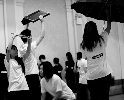 A black and white photo of a group of people that hold different objects above their heads.