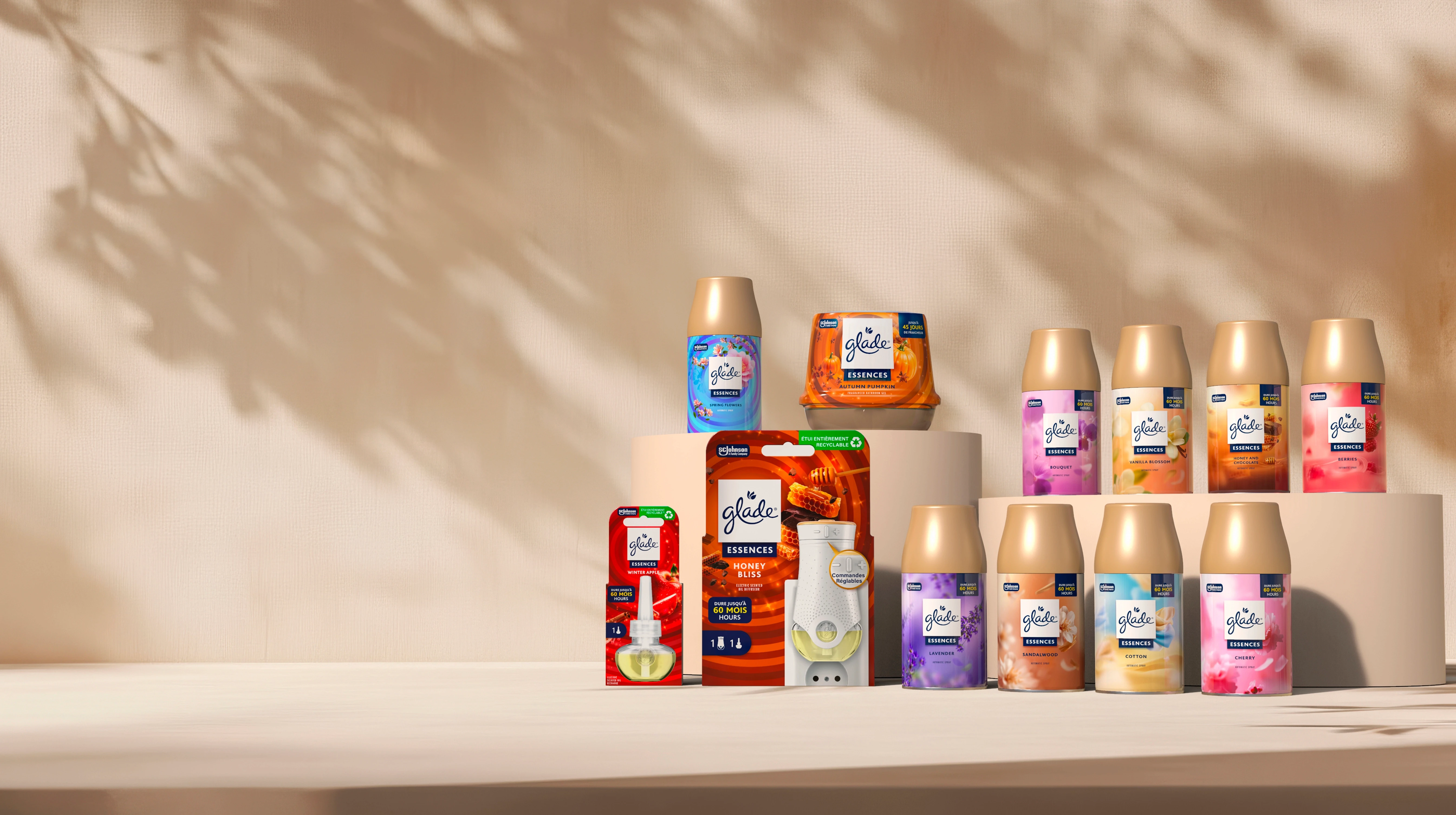 A variety of Glade air freshener products are displayed on a neutral background with soft shadows. The colorful packaging includes sprays, plug-ins, and essential oil bottles.