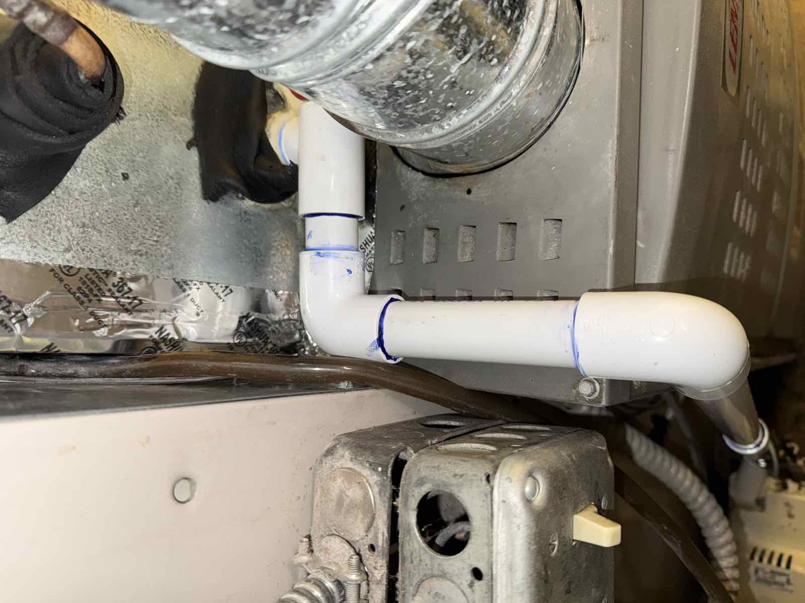 A new white PVC condensate drain line exiting a furnace plenum, replacing the previous fitting.