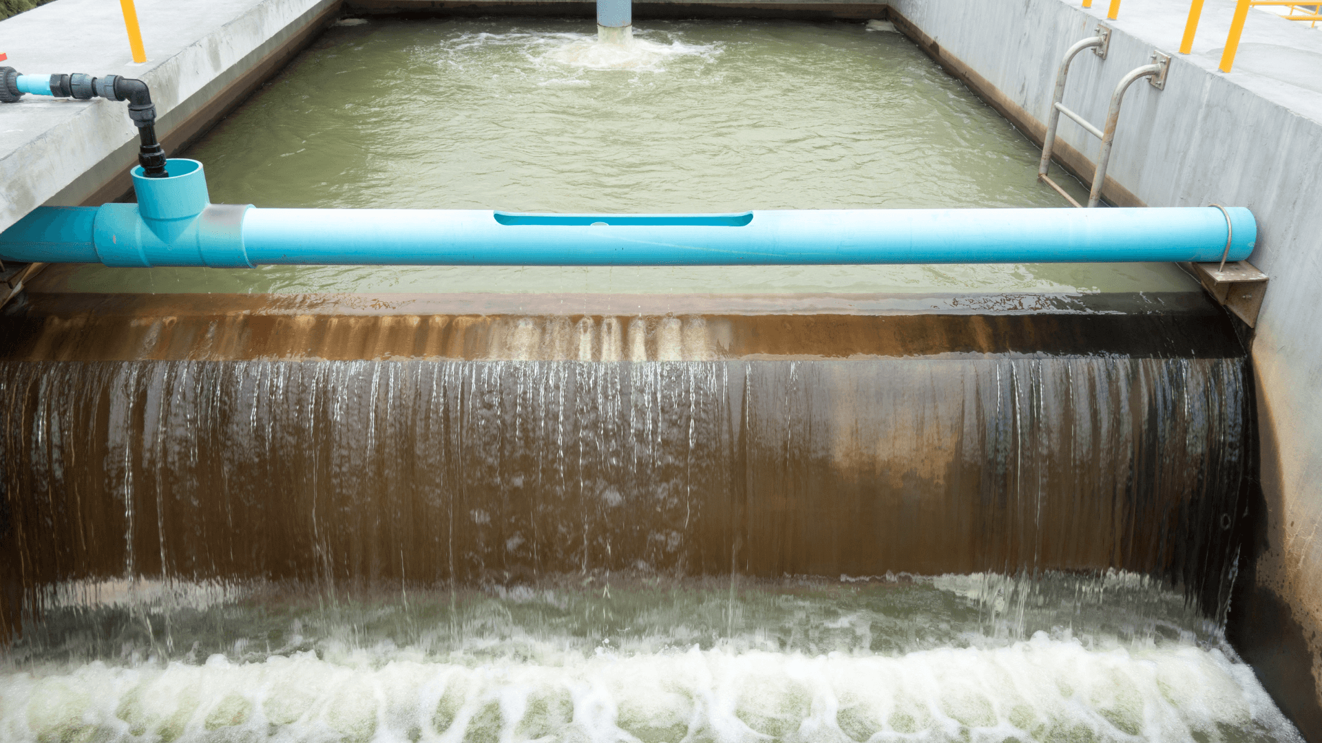 Water cascading over a weir at a water treatment plant, with a blue pipe running across a concrete tank
