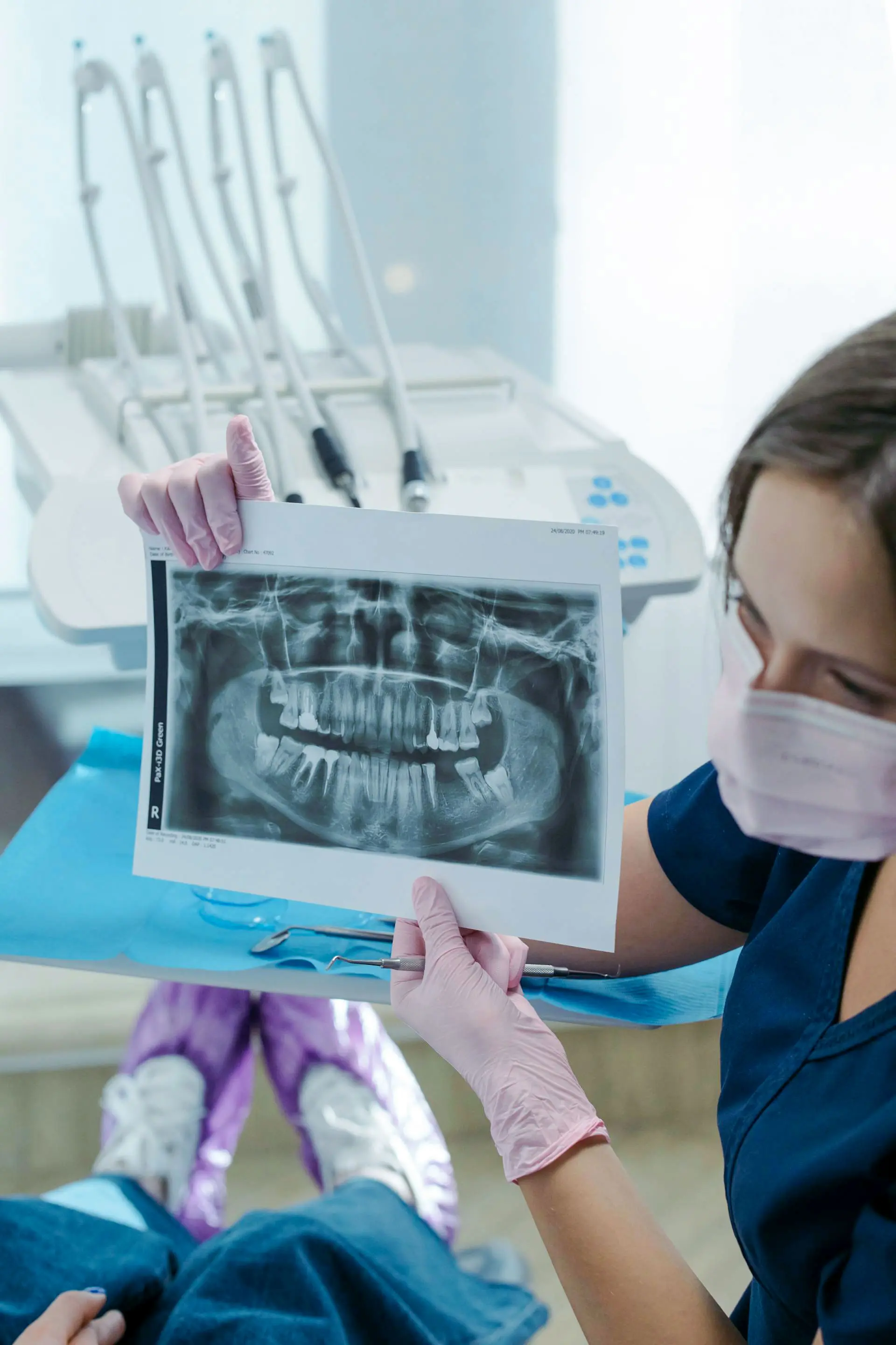 A dental professional examines an X-ray in a clinic while wearing gloves and a mask.
