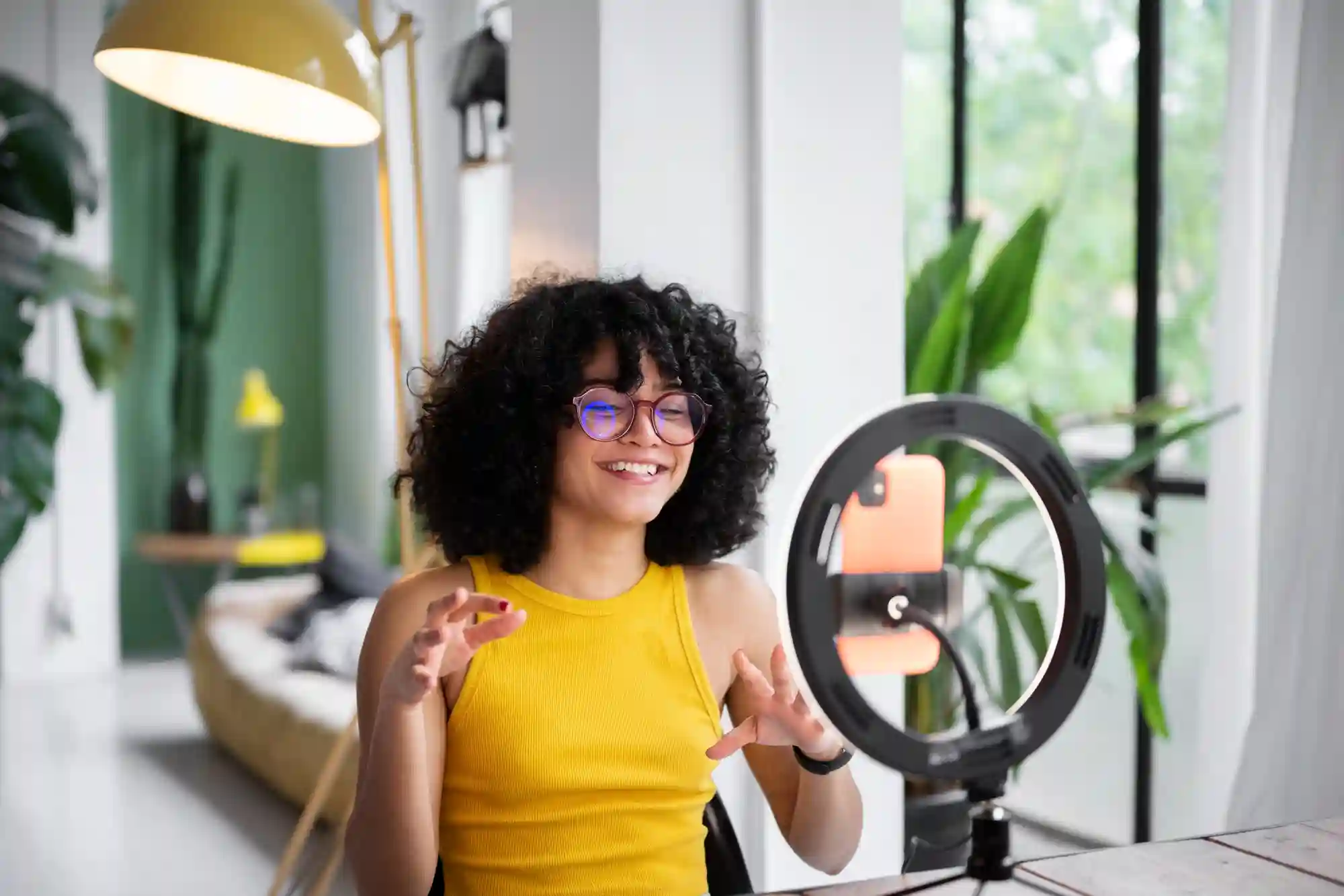 Smiling vlogger recording a tutorial video with a ring light to improve her social media engagement.