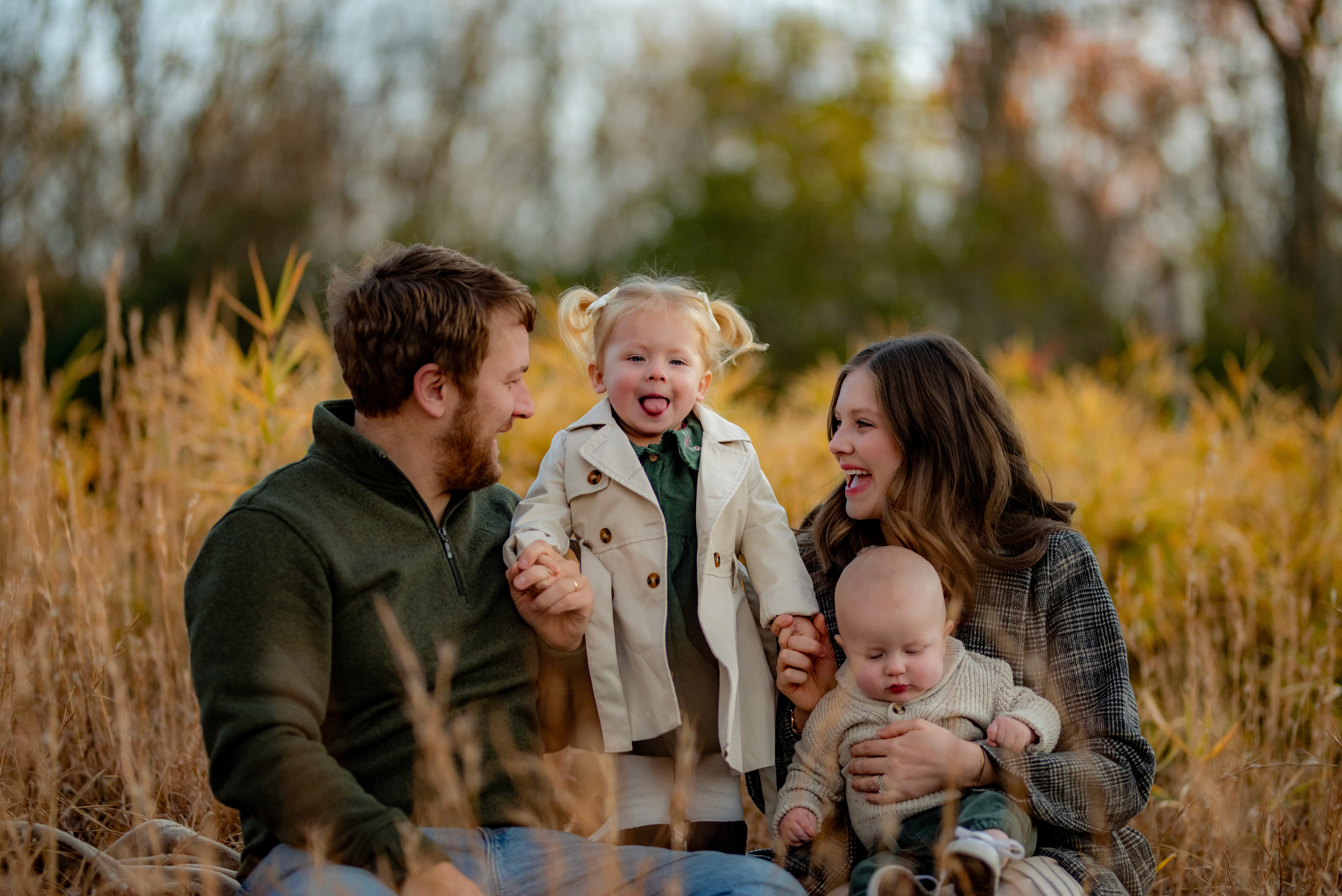 Family portrait with a father, mother, and two children. The daughter sticks her tongue out while being held by her parents.