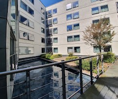 Modern luxury house with glass walls at sunset, overlooking a city skyline. An illuminated pool, palm trees, and indoor-outdoor living space evoke tranquility.