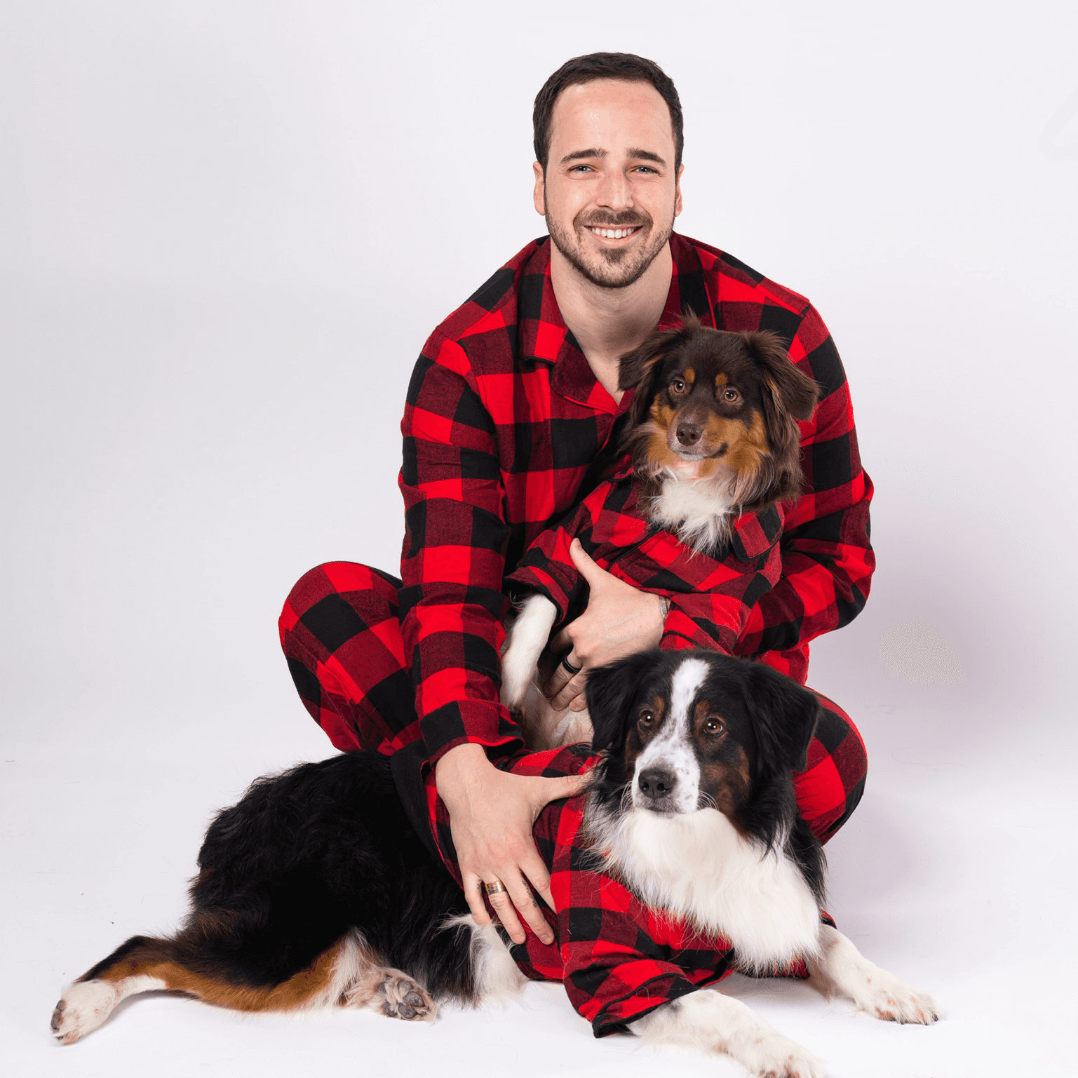 A man and two dogs in matching red and black plaid pajamas smiling at the camera