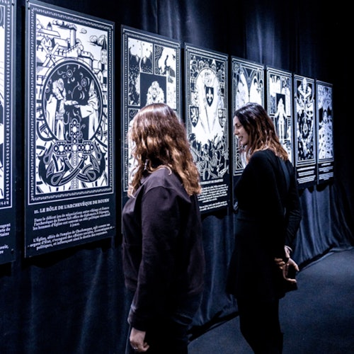 两个人正在参观艺术展览，其中展出了一些展示复杂设计和文字的黑白插图面板。