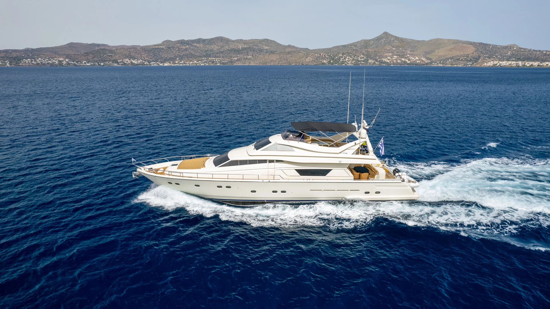 White Rock 36 speedboat with captain at helm cruising calm blue waters near Paros coastline with hills in background.