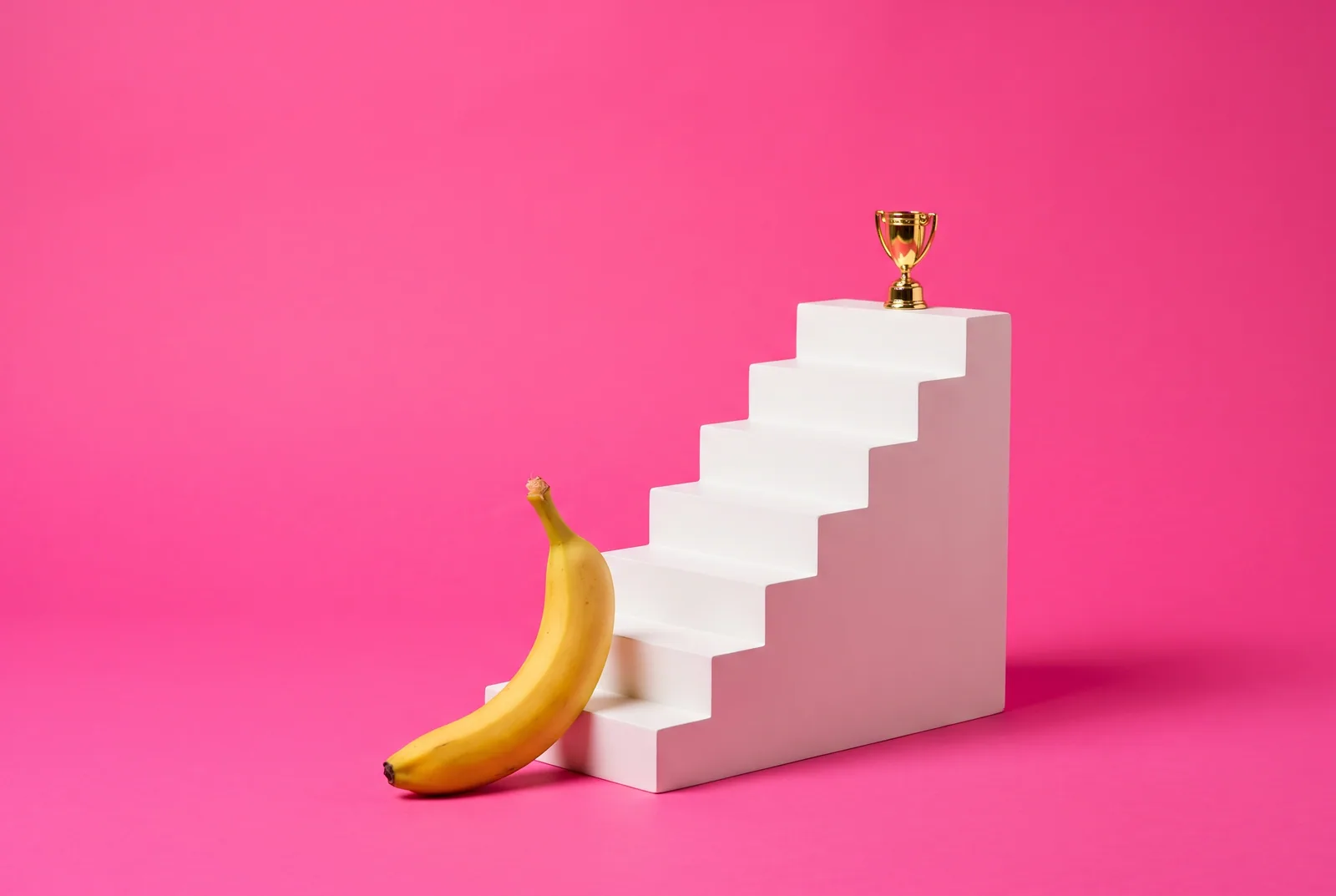 A banana at the foot of seven white steps with a gold trophy on top, a NoFap challenge review for QUITTR vs NoFap