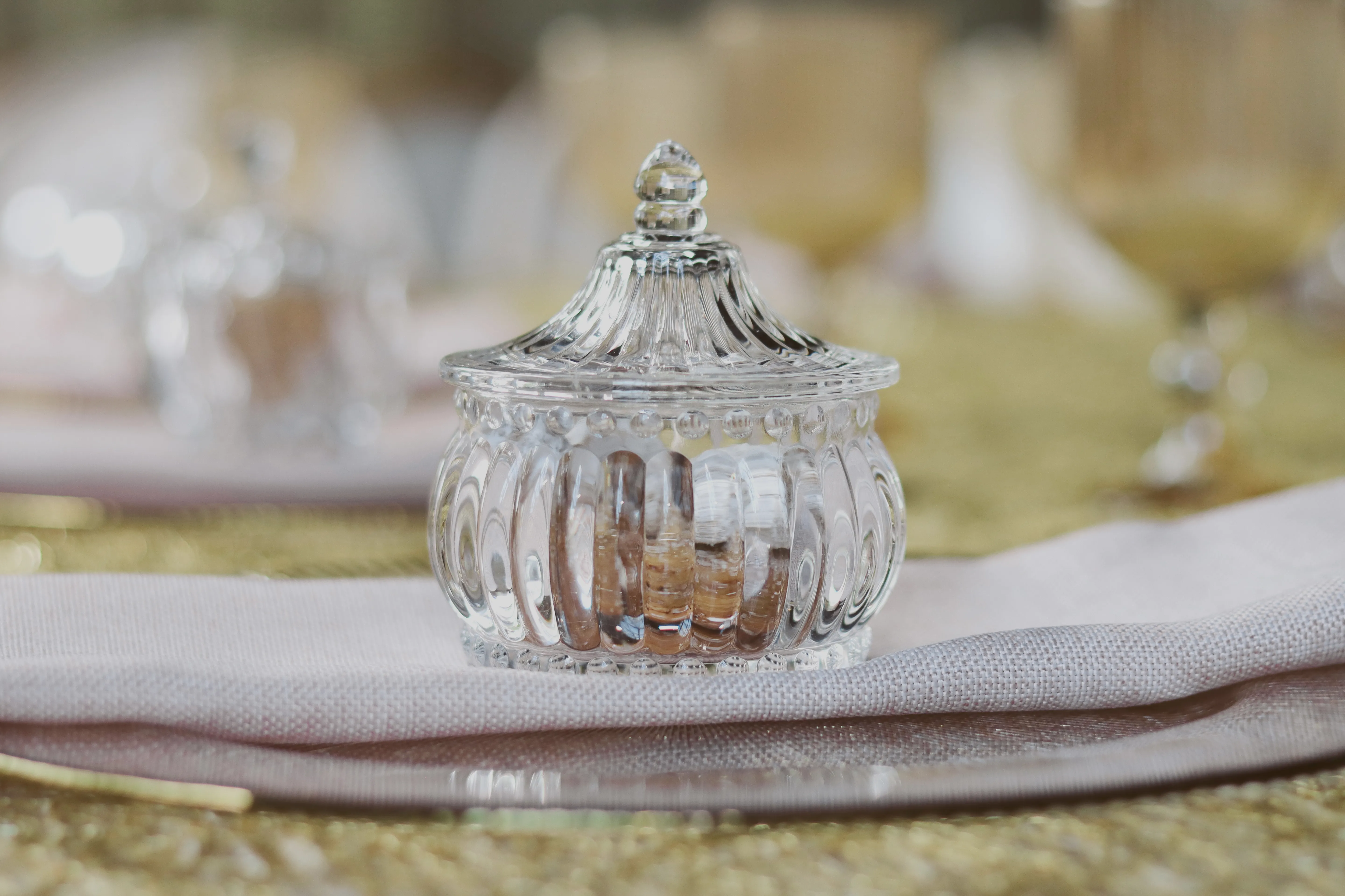 Detalle de frasco de cristal sobre mantel dorado y rosa