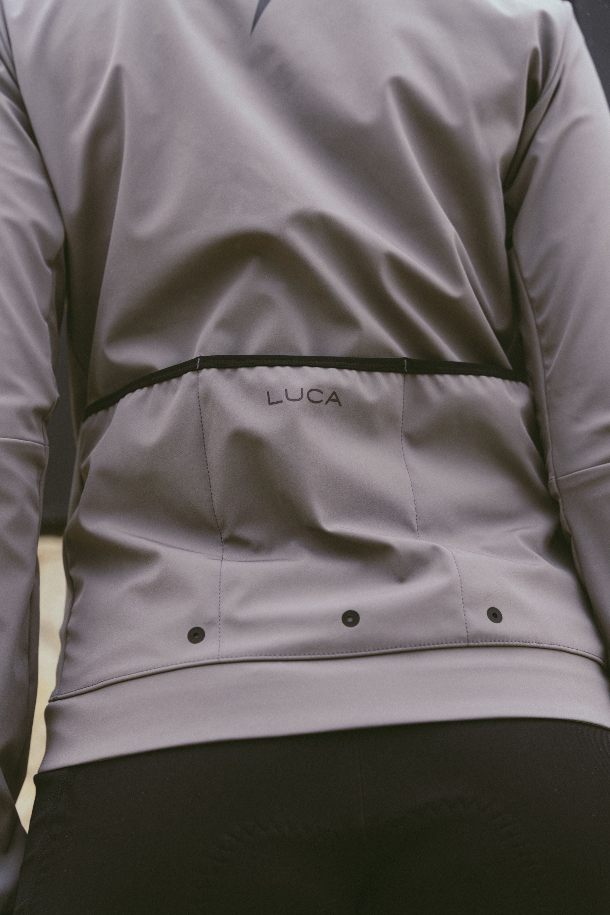 Back-view-of-the-taupe-grey-Luca-cycling-jacket-the-LUCA-logo-and-the-vents-for-temperature-regulation-while-riding