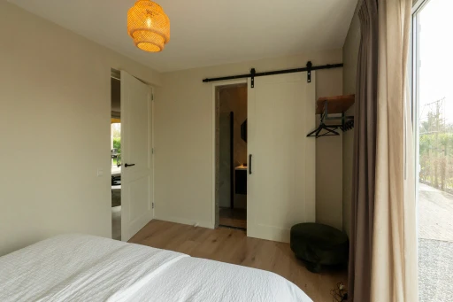 Een slaapkamer met een tweepersoonsbed, een open kapstok en een witte schuifdeur.
