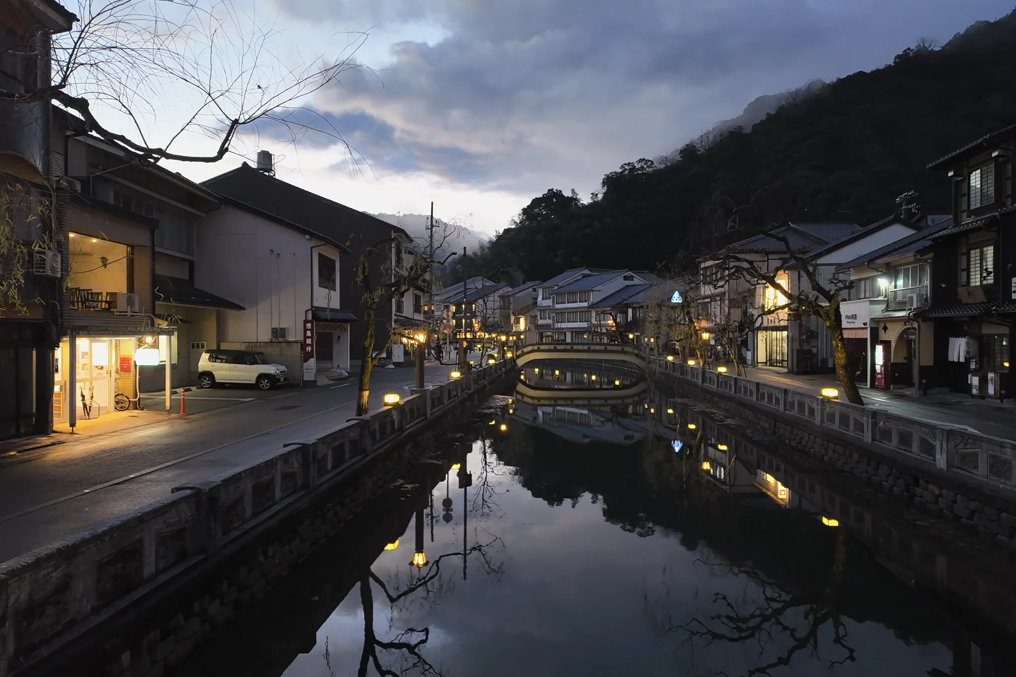 The Kinosaki canal at blue hour, lanterns and inn windows mirrored in still water.