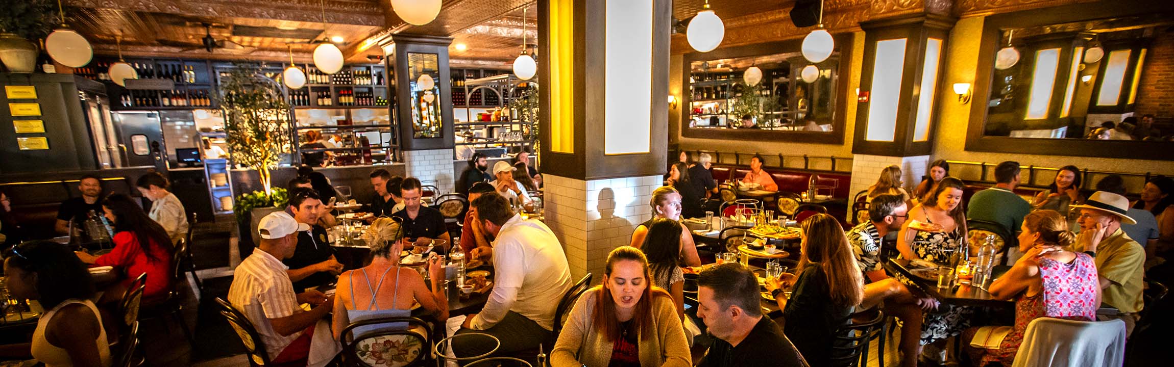 Full dining room of guests at tables under globe lights and a tin ceiling at Marcella's Short North