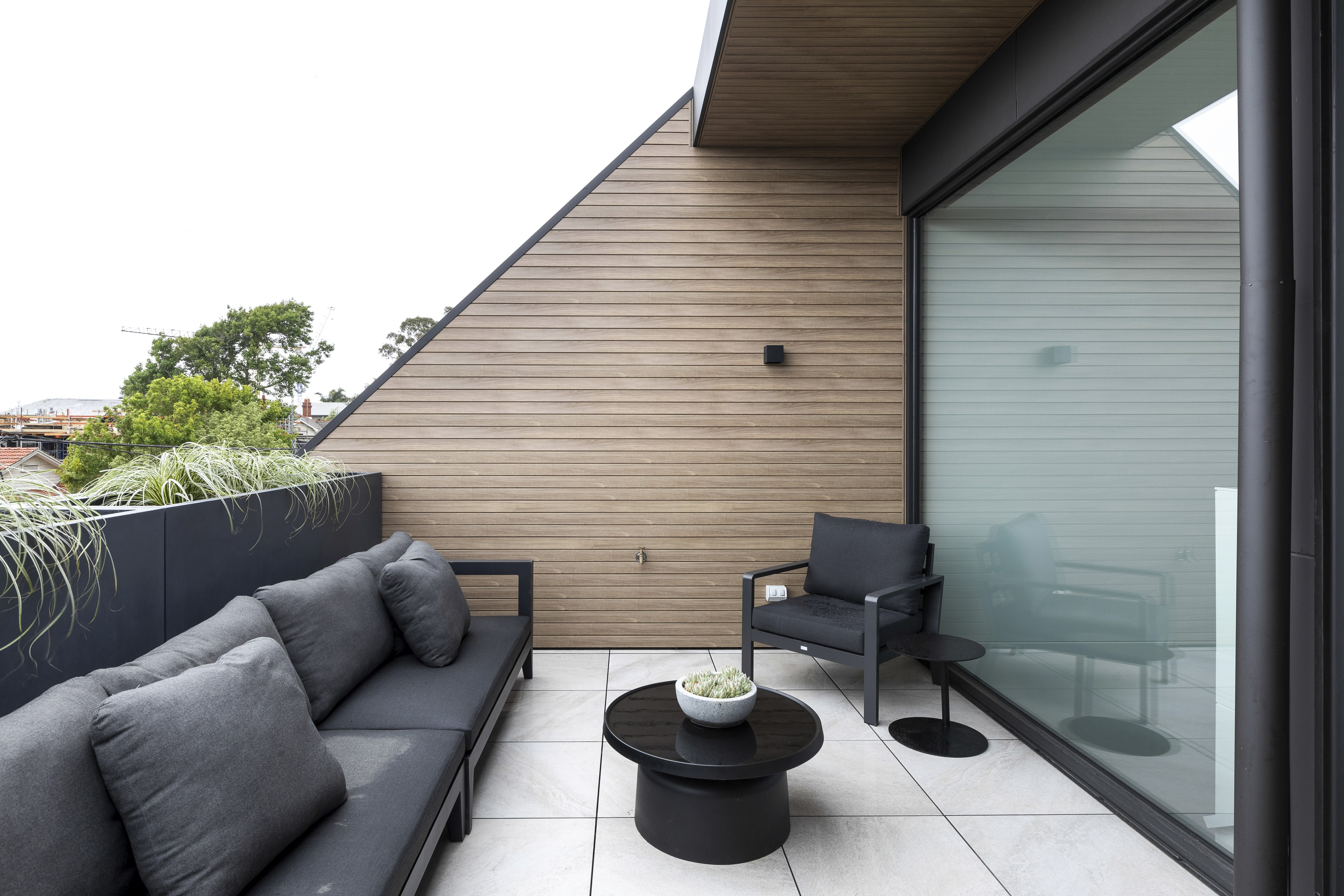 Modern rooftop patio with stylish black furniture and wood paneling.