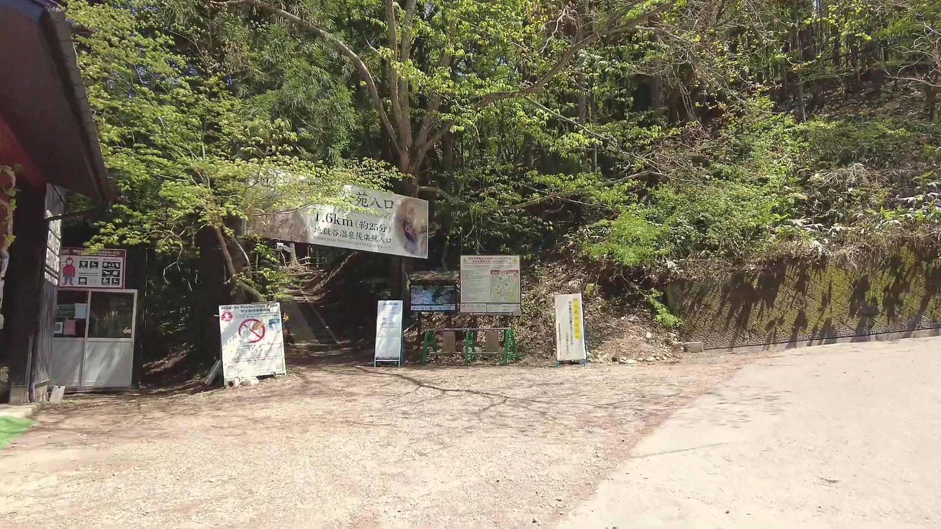 The Jigokudani Monkey Park trailhead in green season — entrance, ticket booth and info boards, with the 1.6 km trail sign.