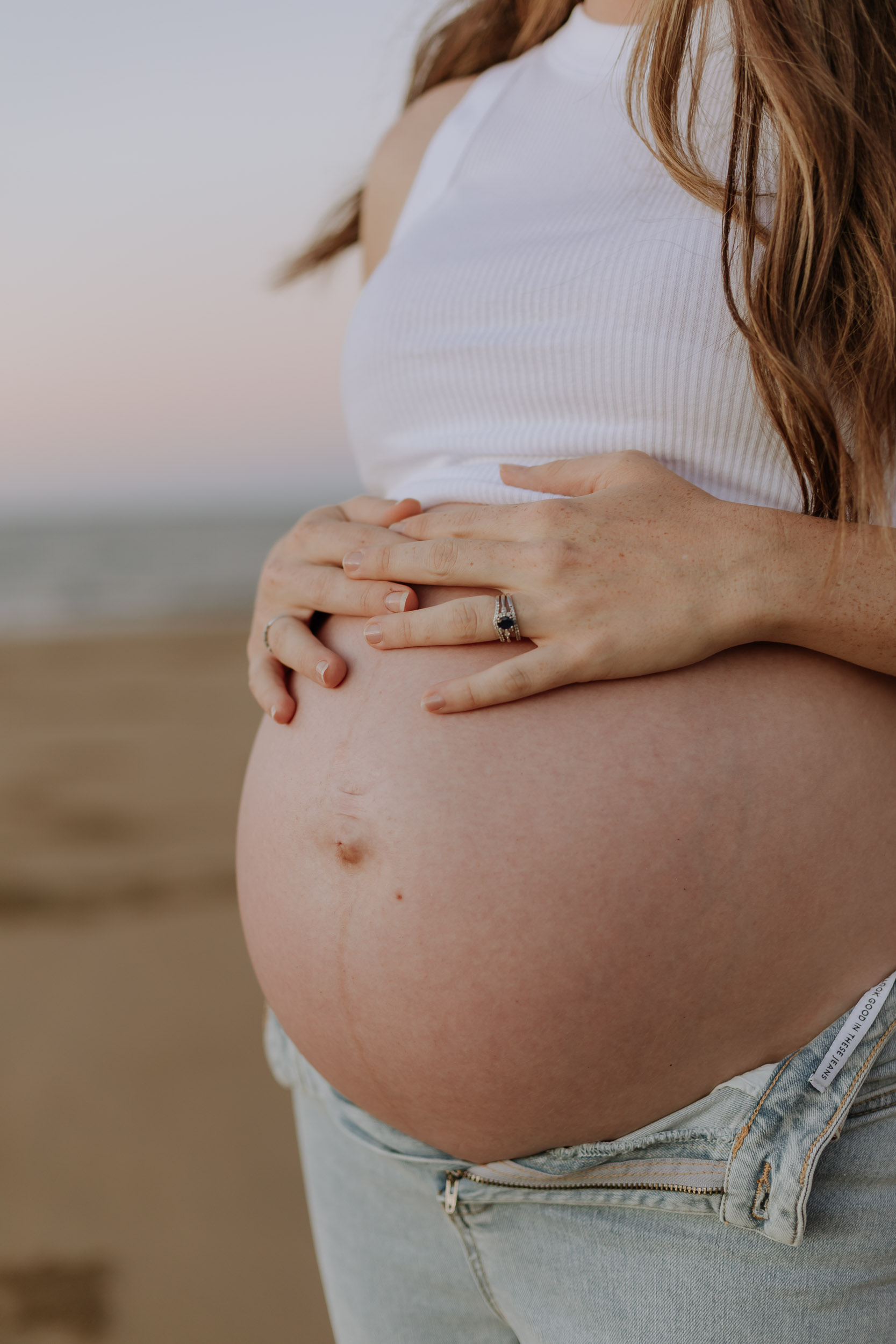 Close up of mother holding her pregnant belly at the beach at sunset