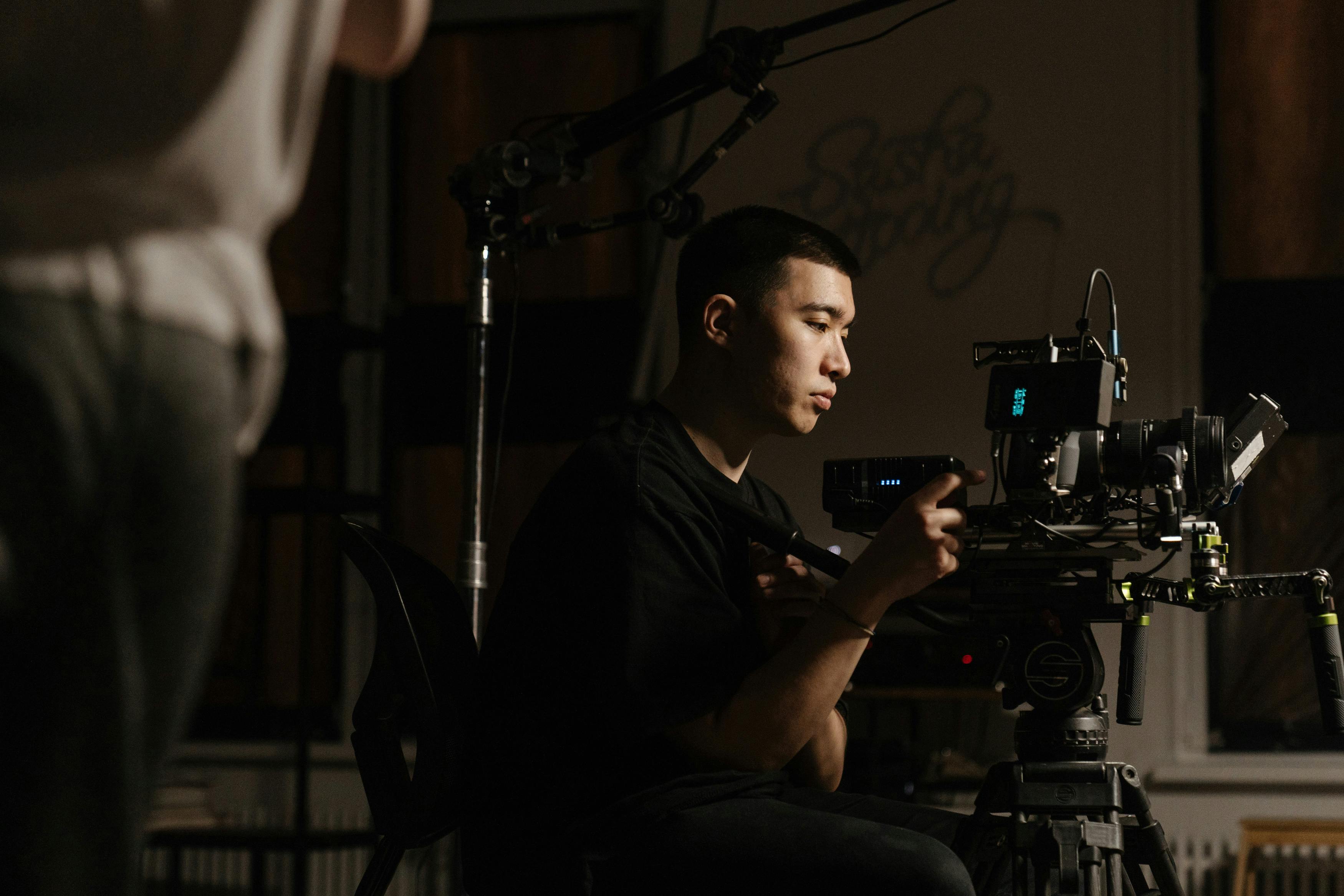 a director and a producer discuss a scene on a bustling film set, with crew members operating cameras and lighting equipment in the background.