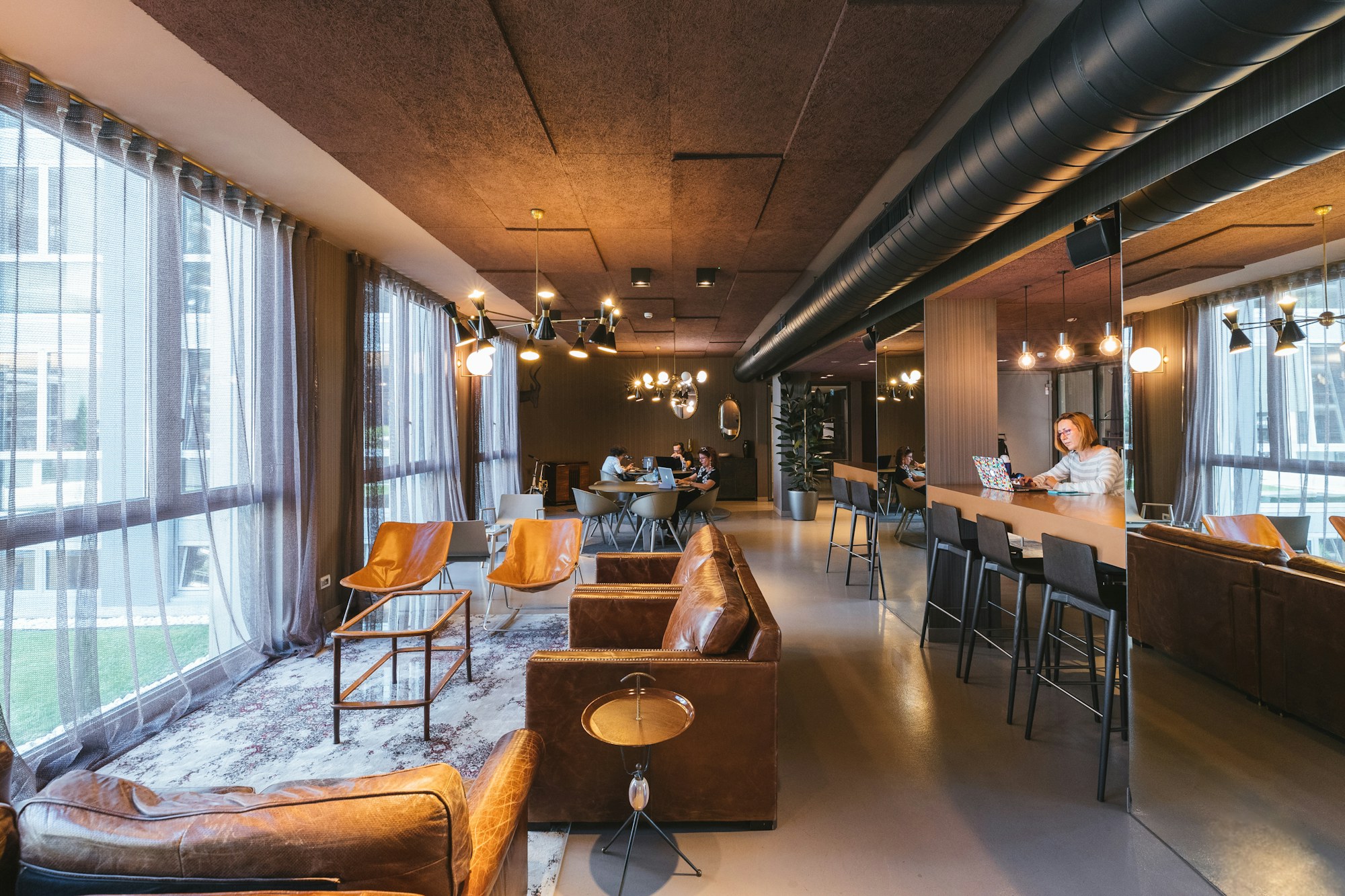 A lounge with leather sofas, a long coffee bar and tall windows