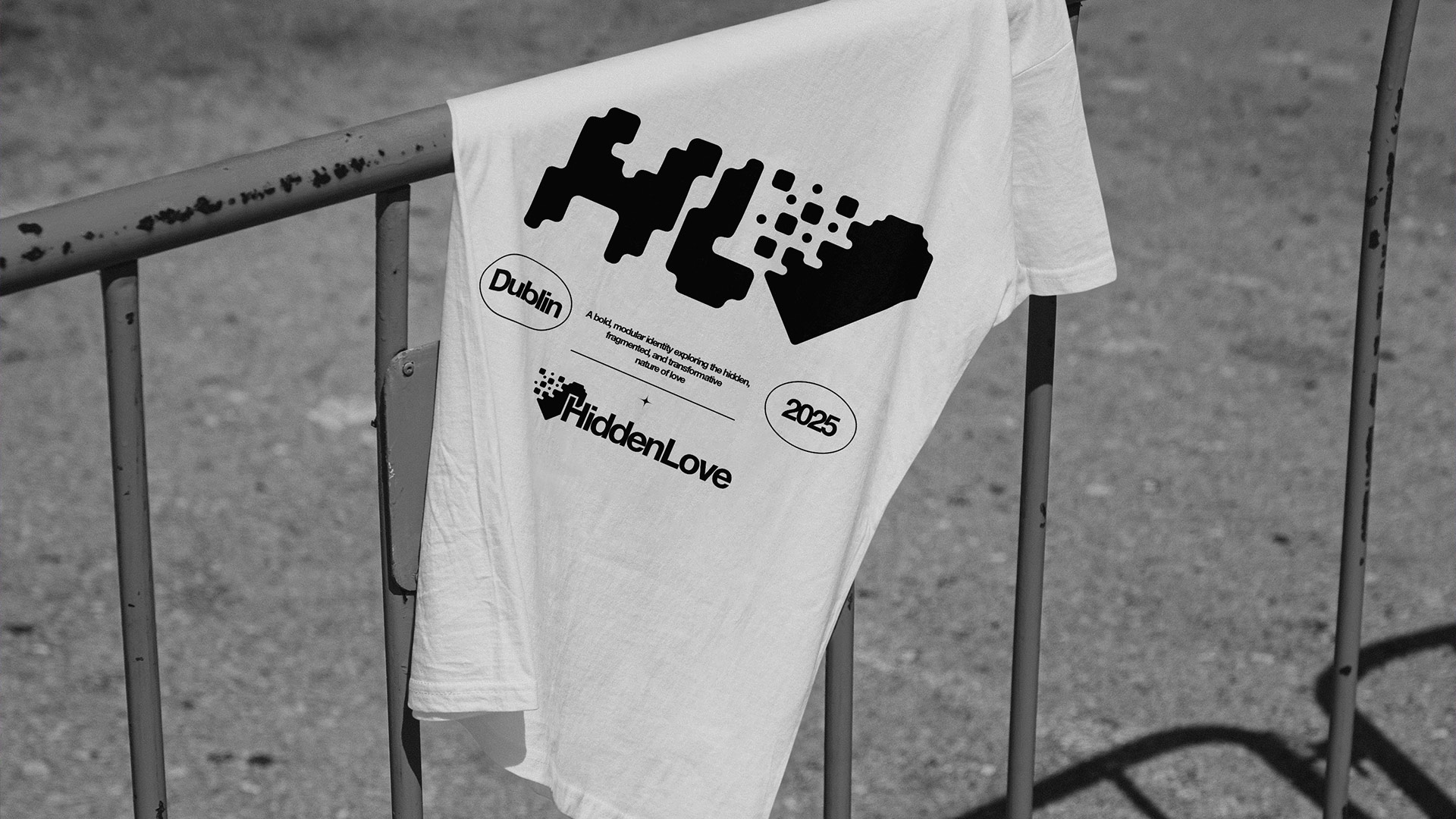 White T-shirt with bold black Hidden Love graphic draped over a metal fence.