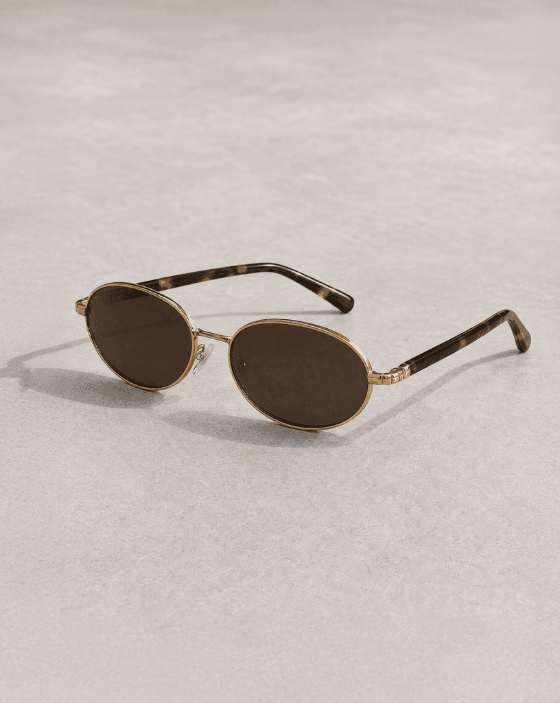 Glossy black Riviera sunglasses photographed on warm ivory limestone.