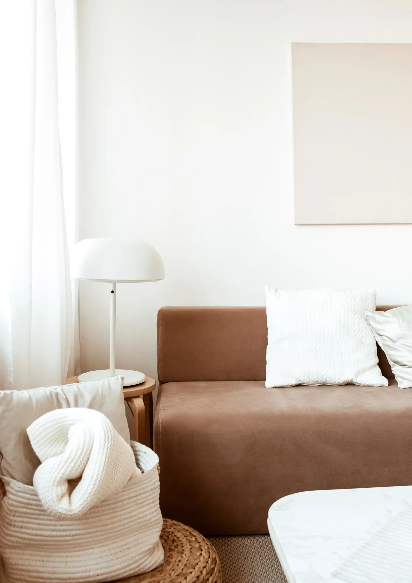 Un canapé marron avec des coussins balncs, une table basse et une lampe.