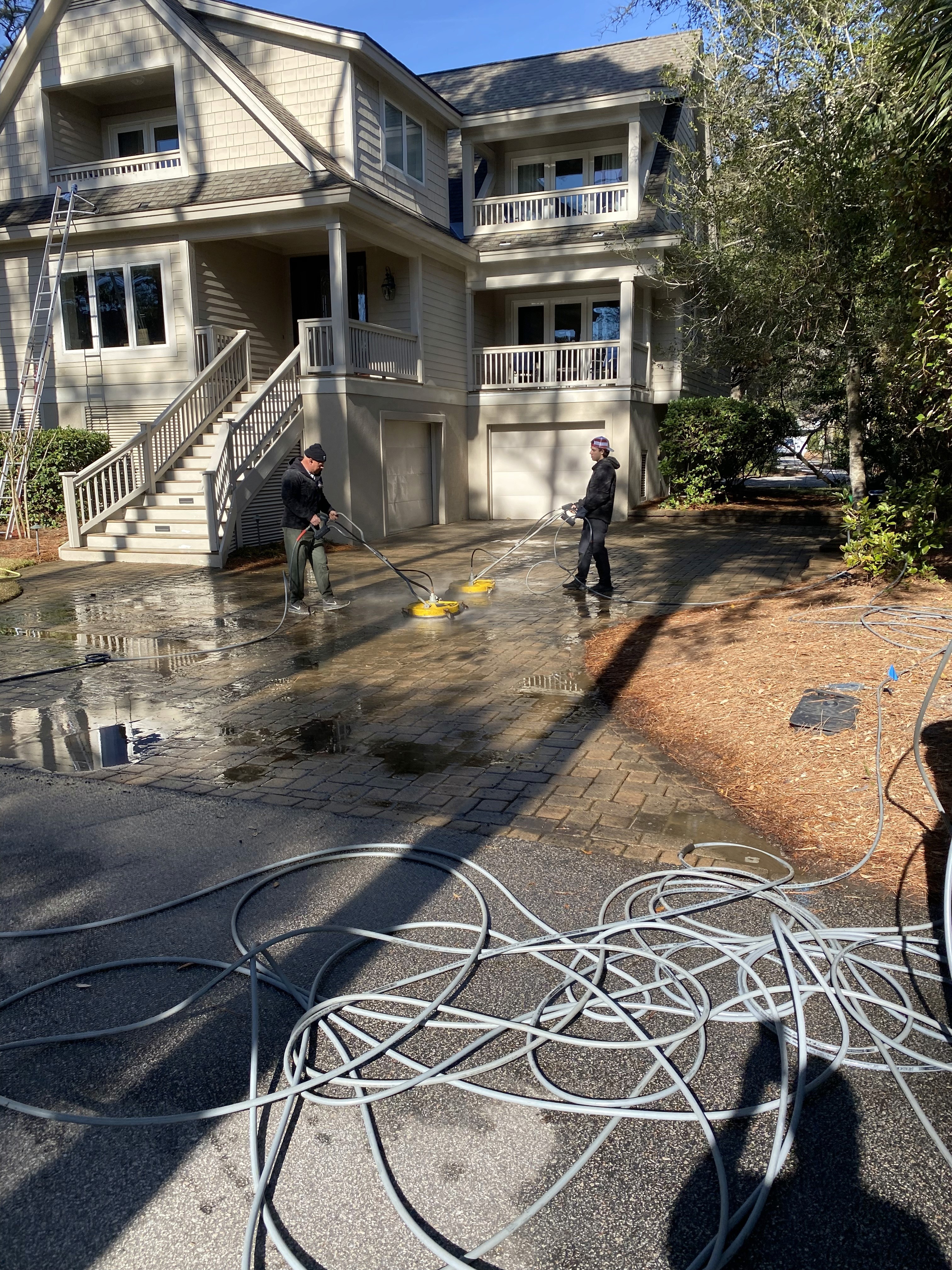Technician using soft/power washing equipment—hose and spray applied to home exterior