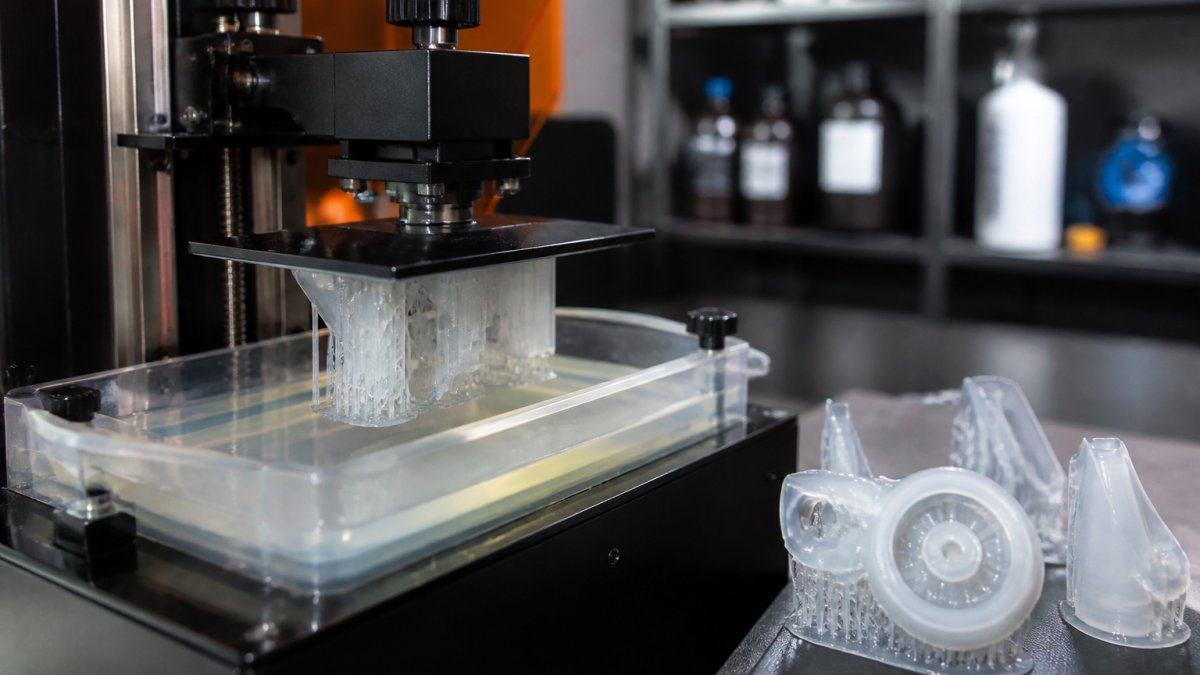 3D printer nozzle depositing resin layers with finished parts nearby to illustrate 3D printing vs injection moulding