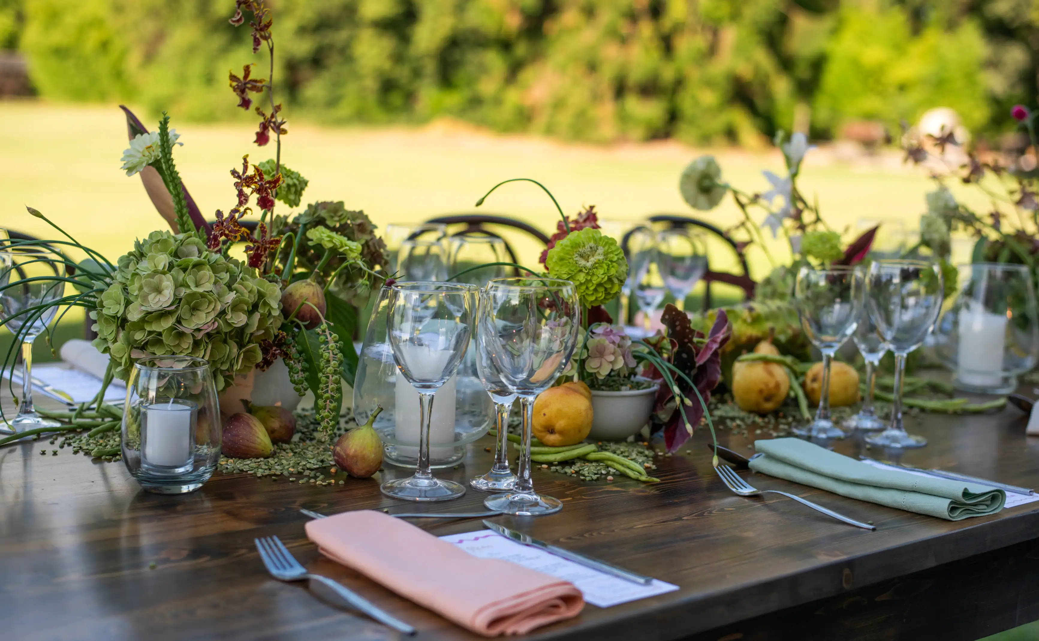 Mesa al aire libre con centro de flores y frutas frescas en tonos verdes y amarillos para evento campestre, evocando frescura orgánica.