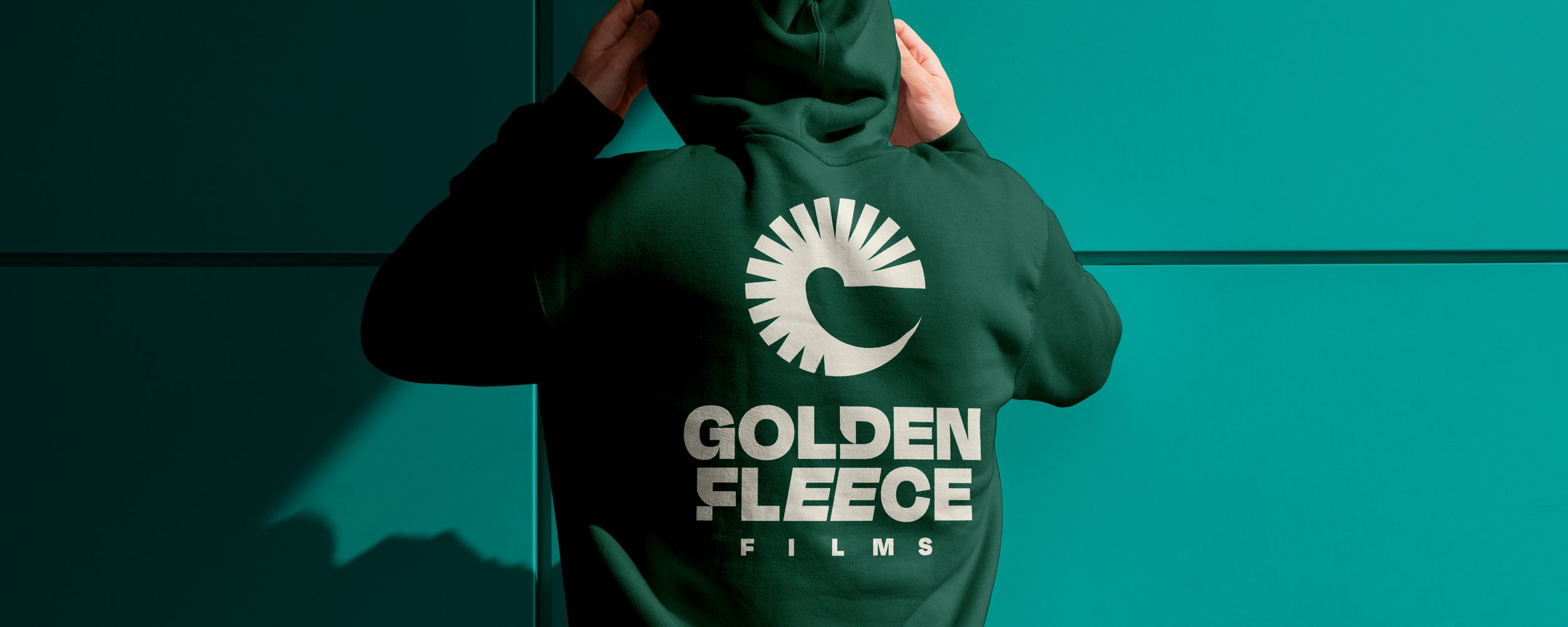 Person wearing a dark green hoodie featuring the Golden Fleece Films logo and bold white typography against a teal background.