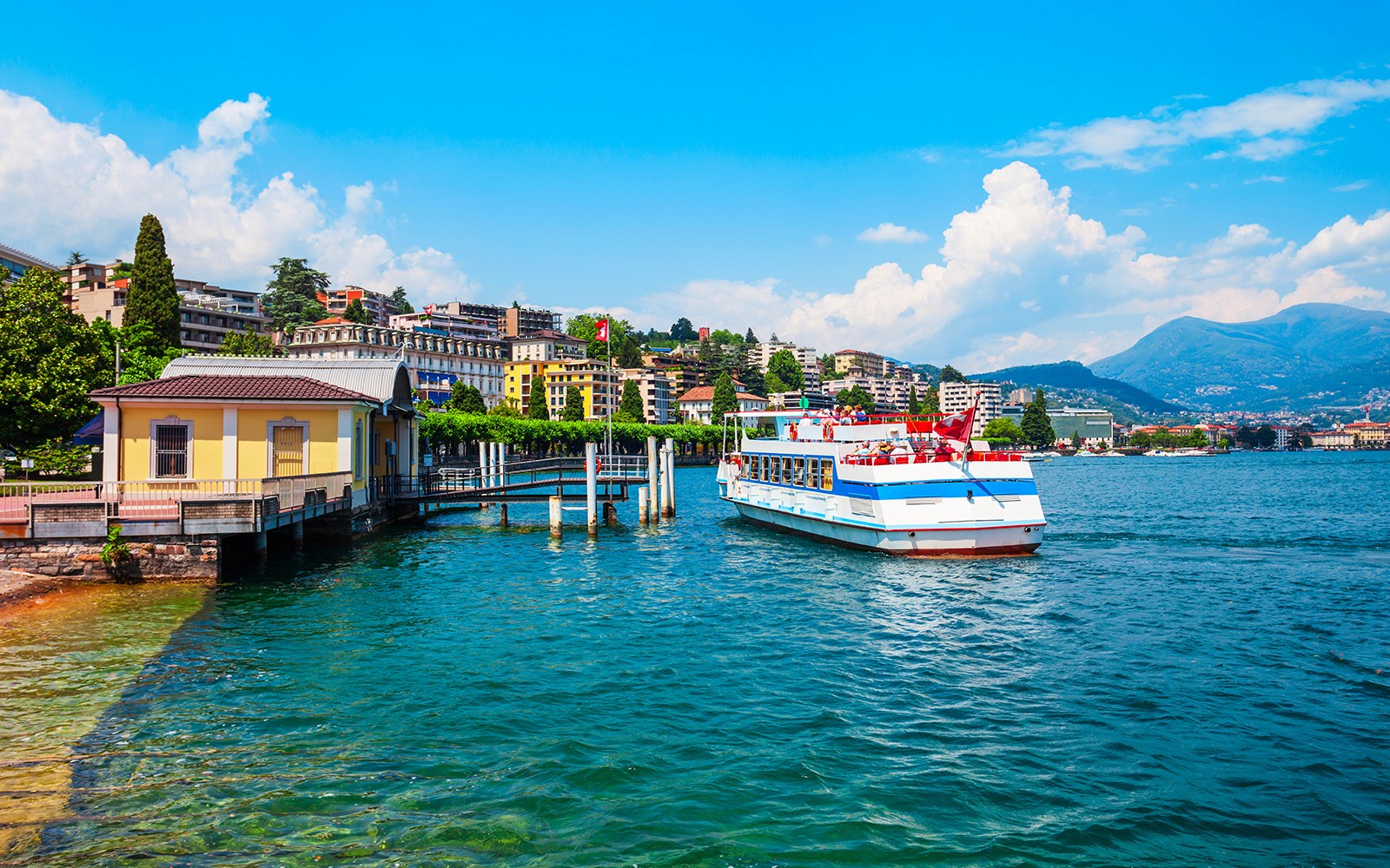 Croisière en bateau sur le lac de Lugano avec panorama urbain et montagnes en arrière-plan.