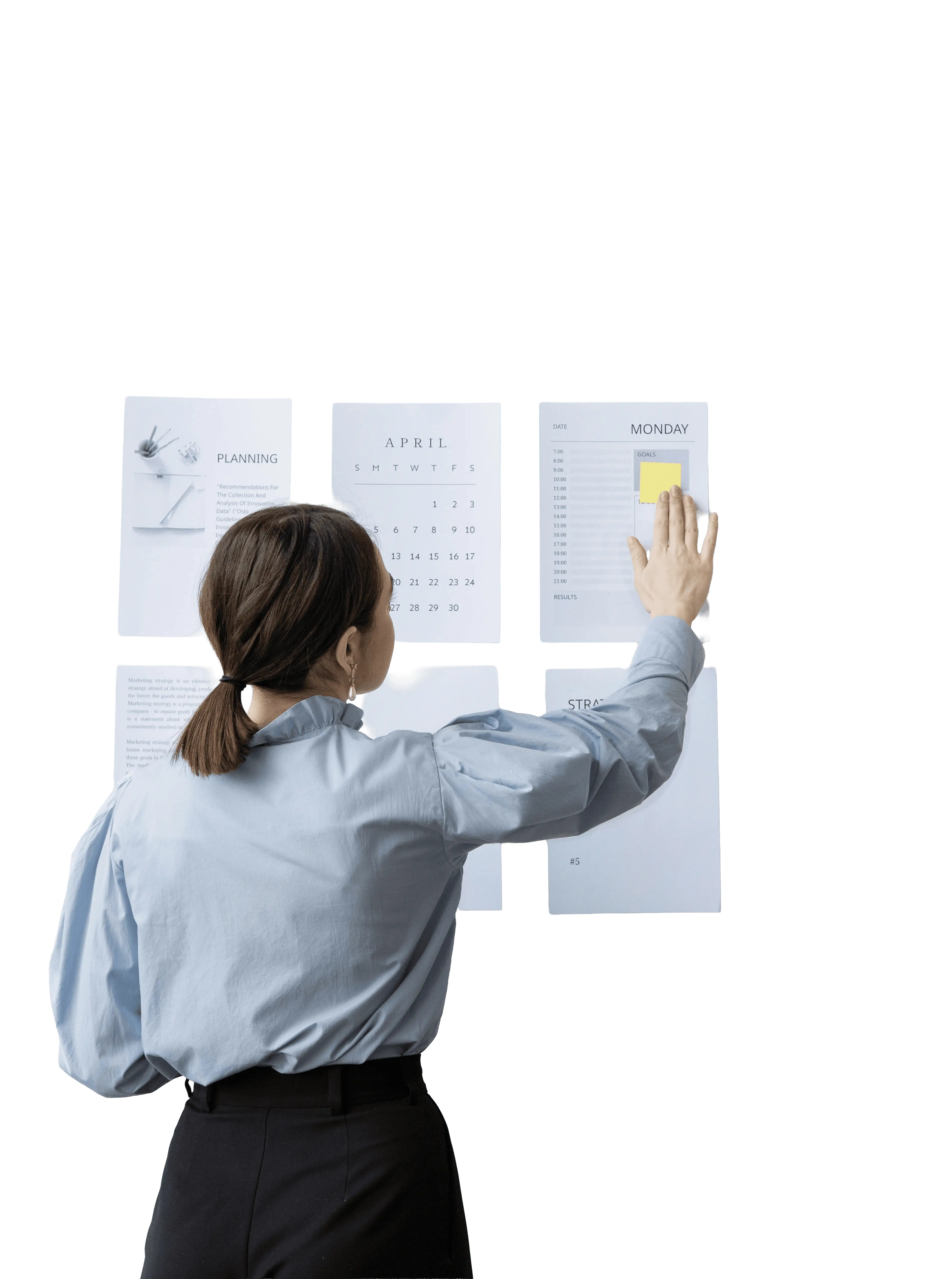 A woman in a blue shirt standing with her back to the camera, organizing planning sheets on a wall.
