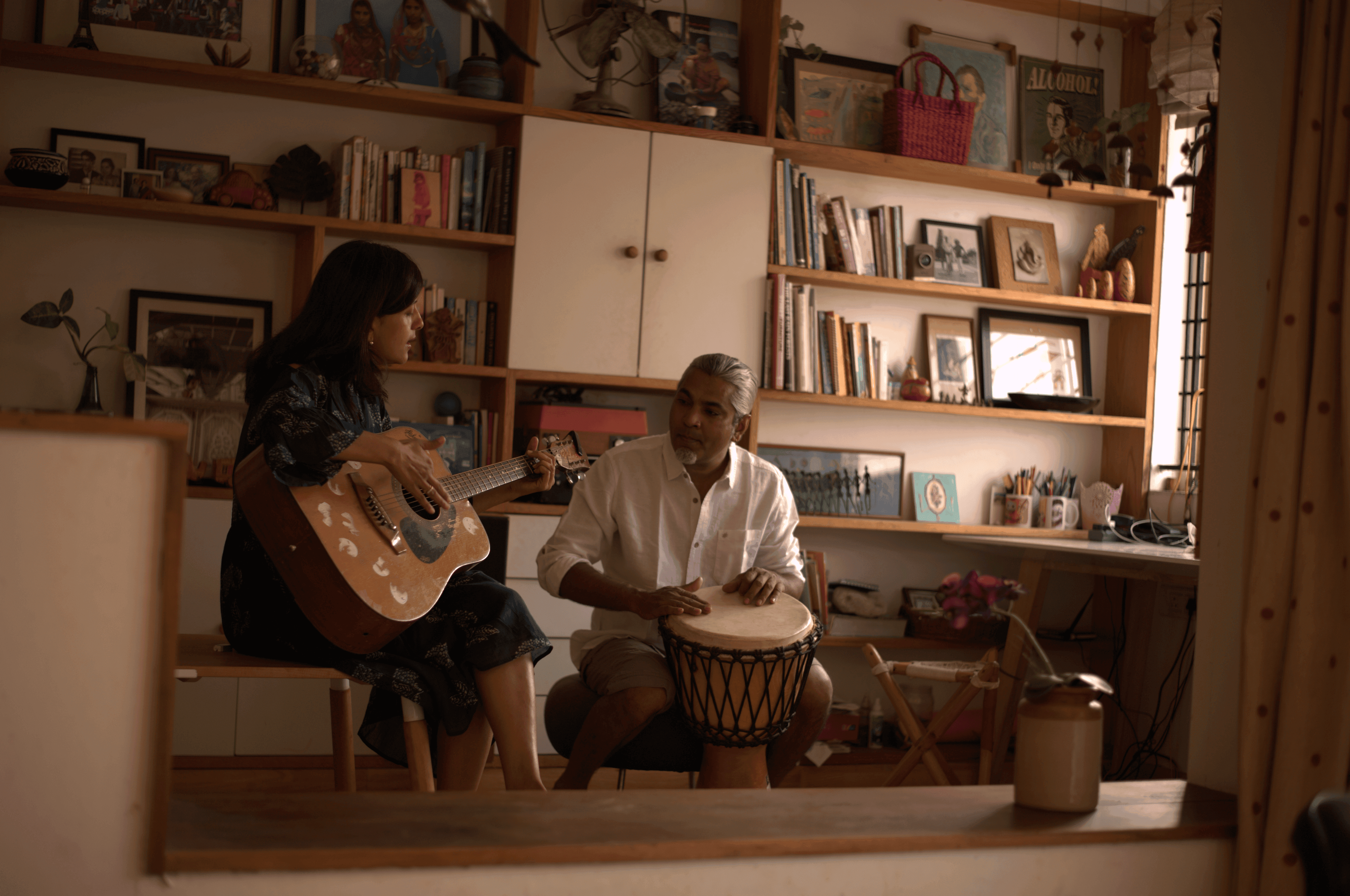 A couple in wedding attire walks hand in hand across a sunlit field.