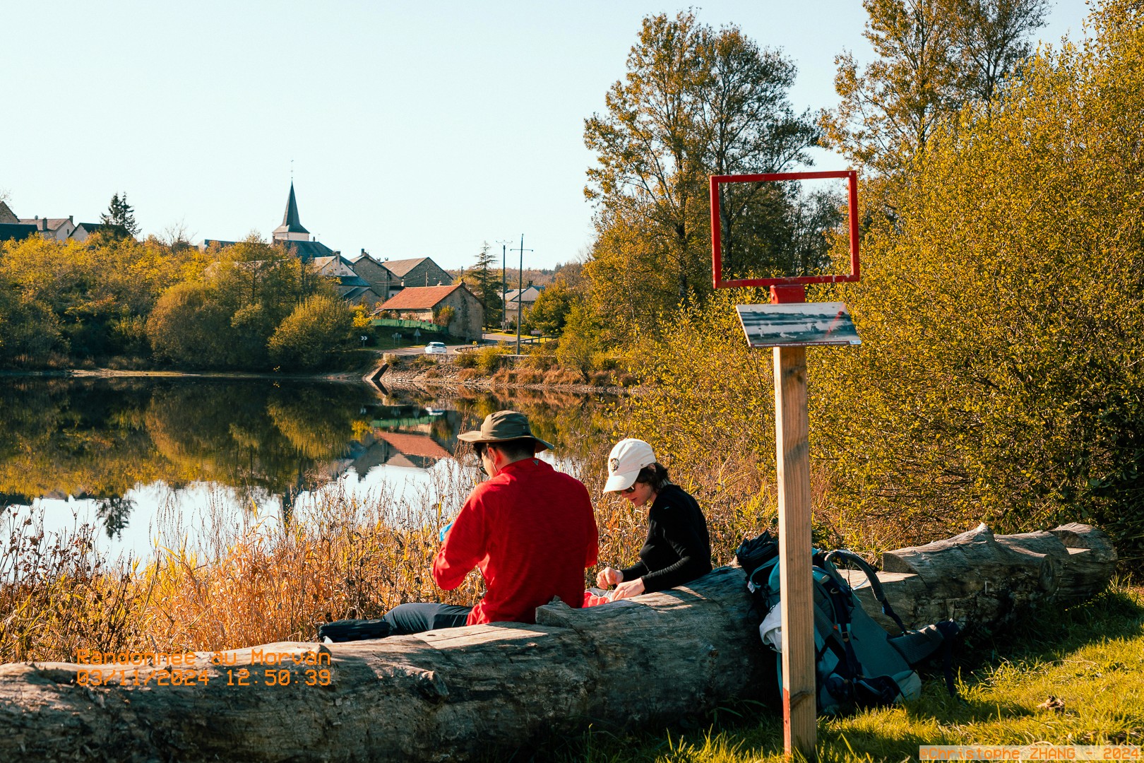 Scène de détente en bord de lac, entourée de végétation automnale et vue sur des maisons du Morvan.
