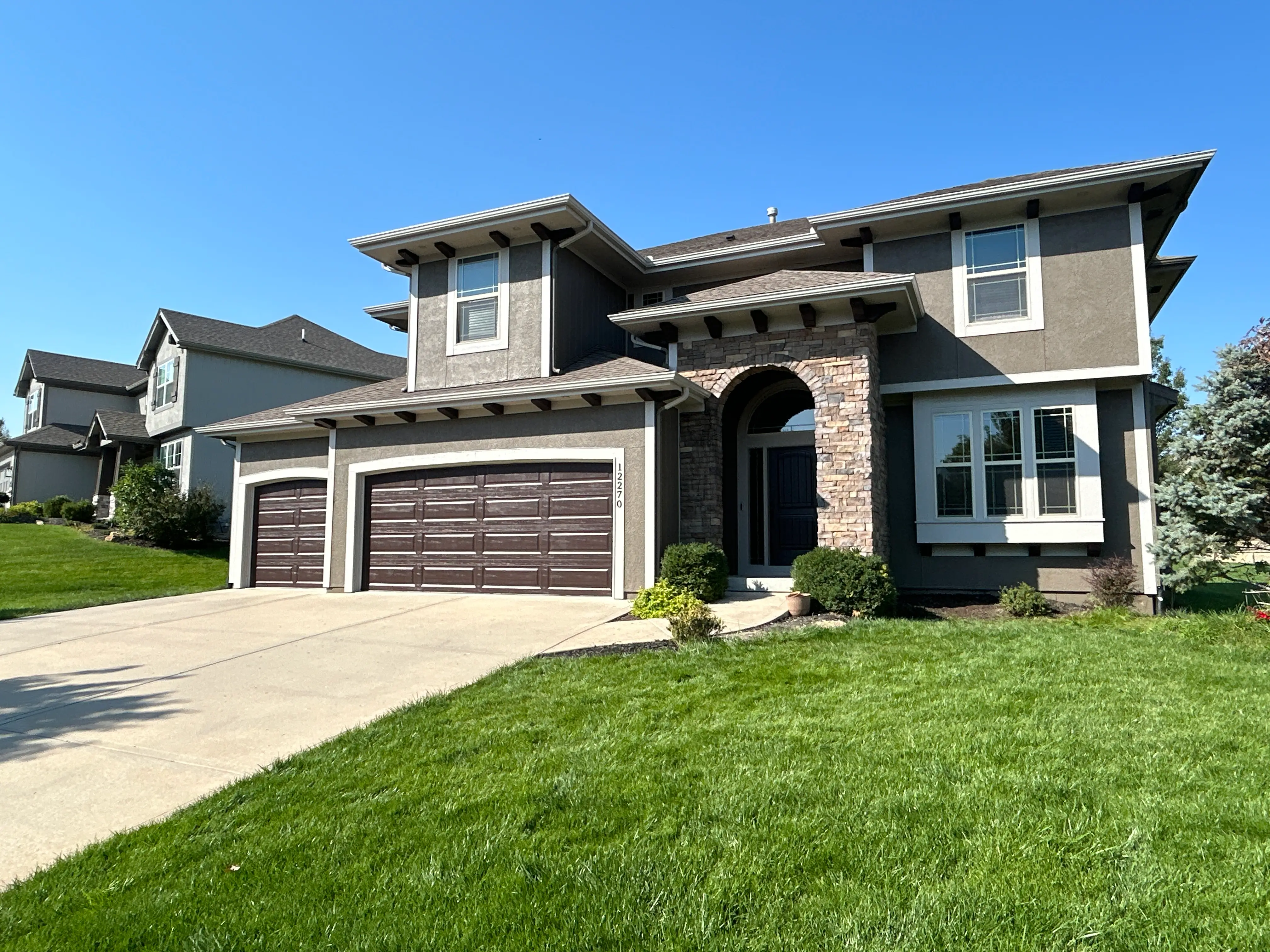 An image of a tan house with white trim and a dark brown garage door.