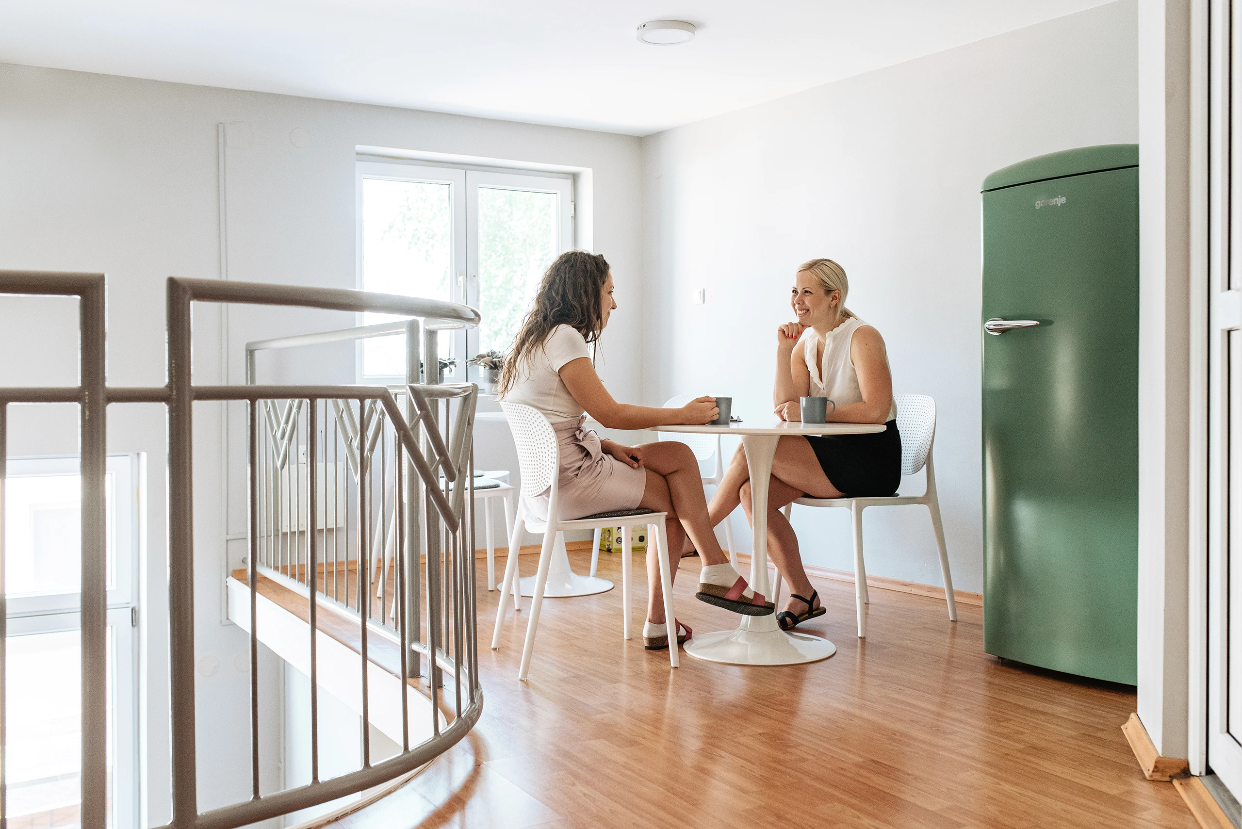 Colleagues having a casual coffee break and conversation in a bright office space.