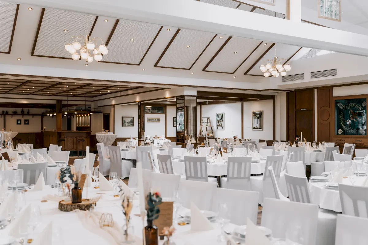 Festlich gedeckter Saal mit Tischen und Stühlen. Dekoration mit Blumen und Holz auf dem Tisch. Moderne Kronleuchter.