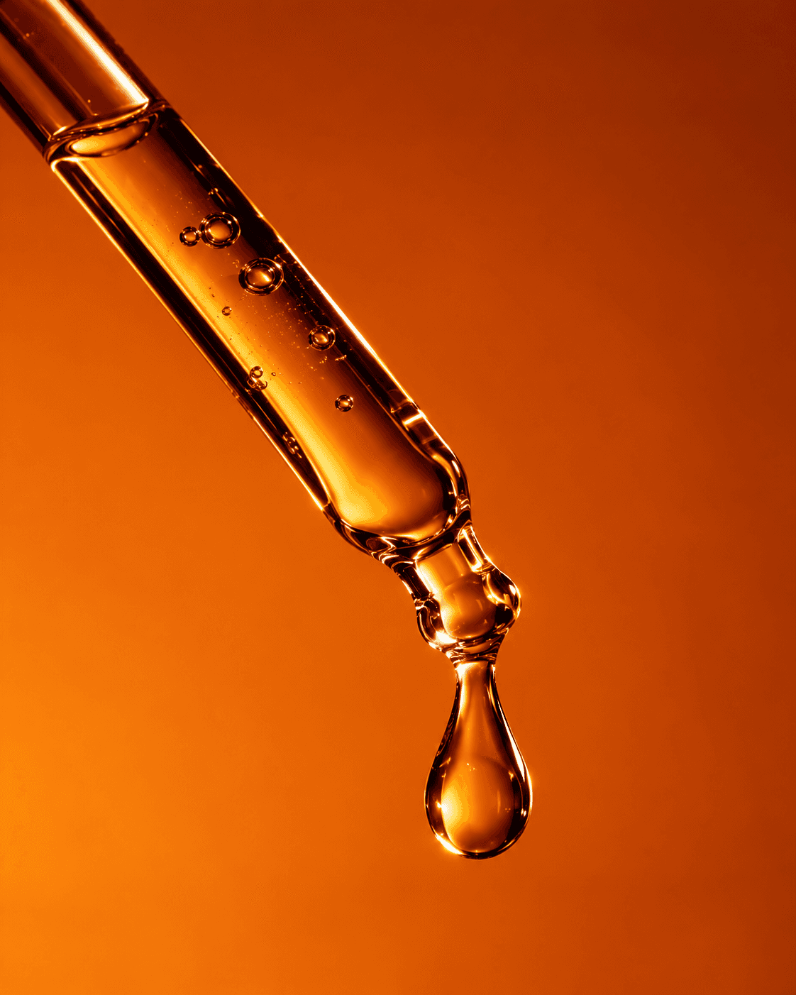 Amber drop falling from a glass pipette on orange