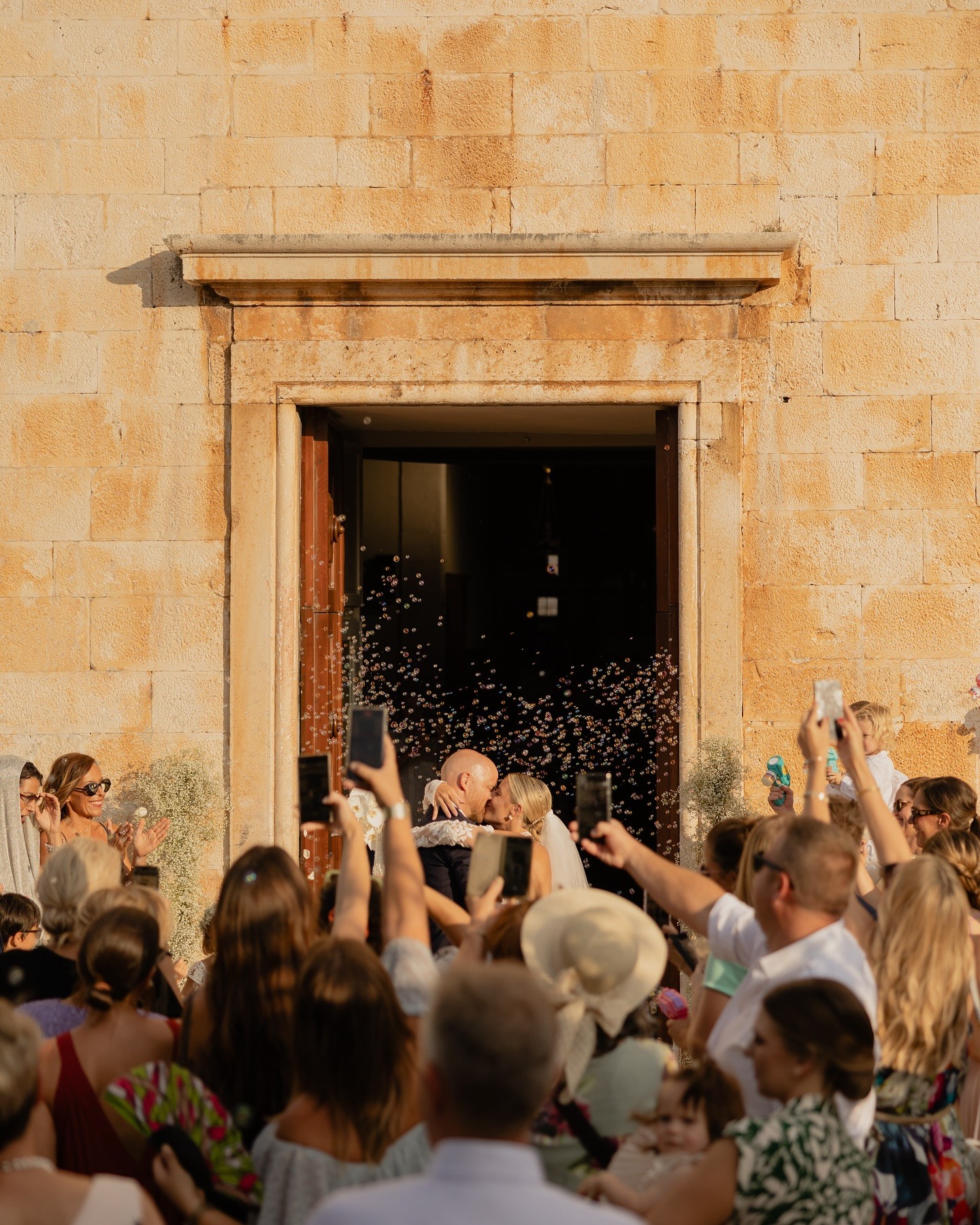 Newly wedded couple kissing and embracing infront of the open door of an old stone church