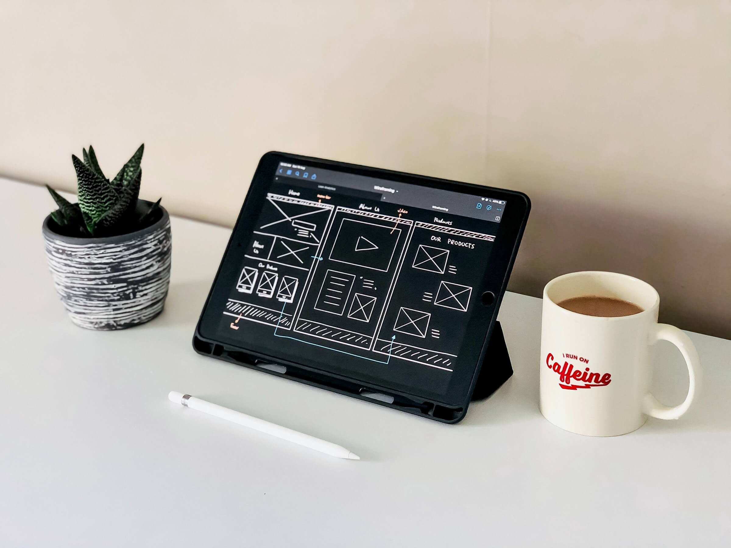 Tablet displaying website wireframe sketches beside a plant and a mug of coffee