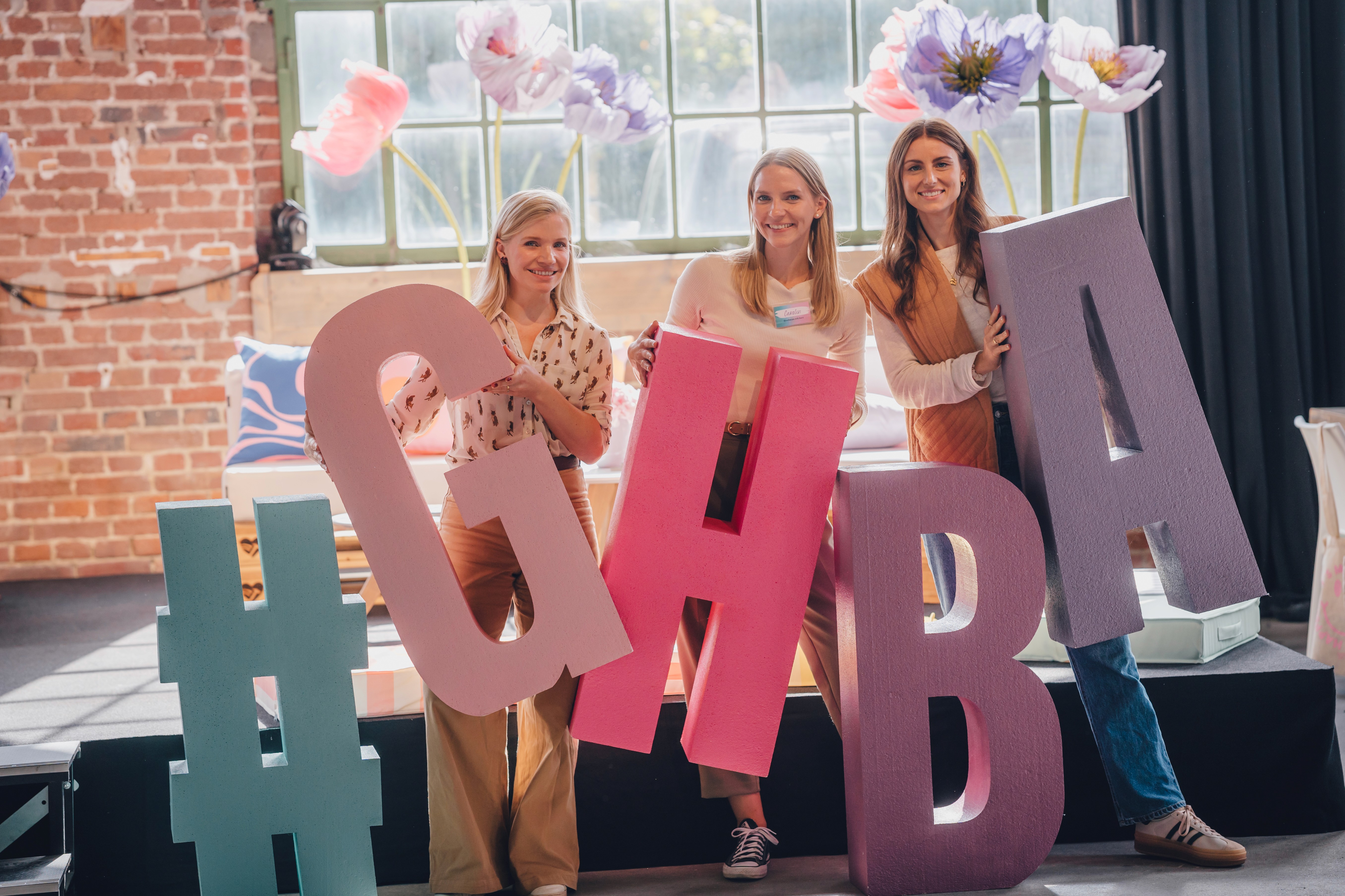 Vier Frauen halten große Buchstaben #GHBA in der Eventlocation. 