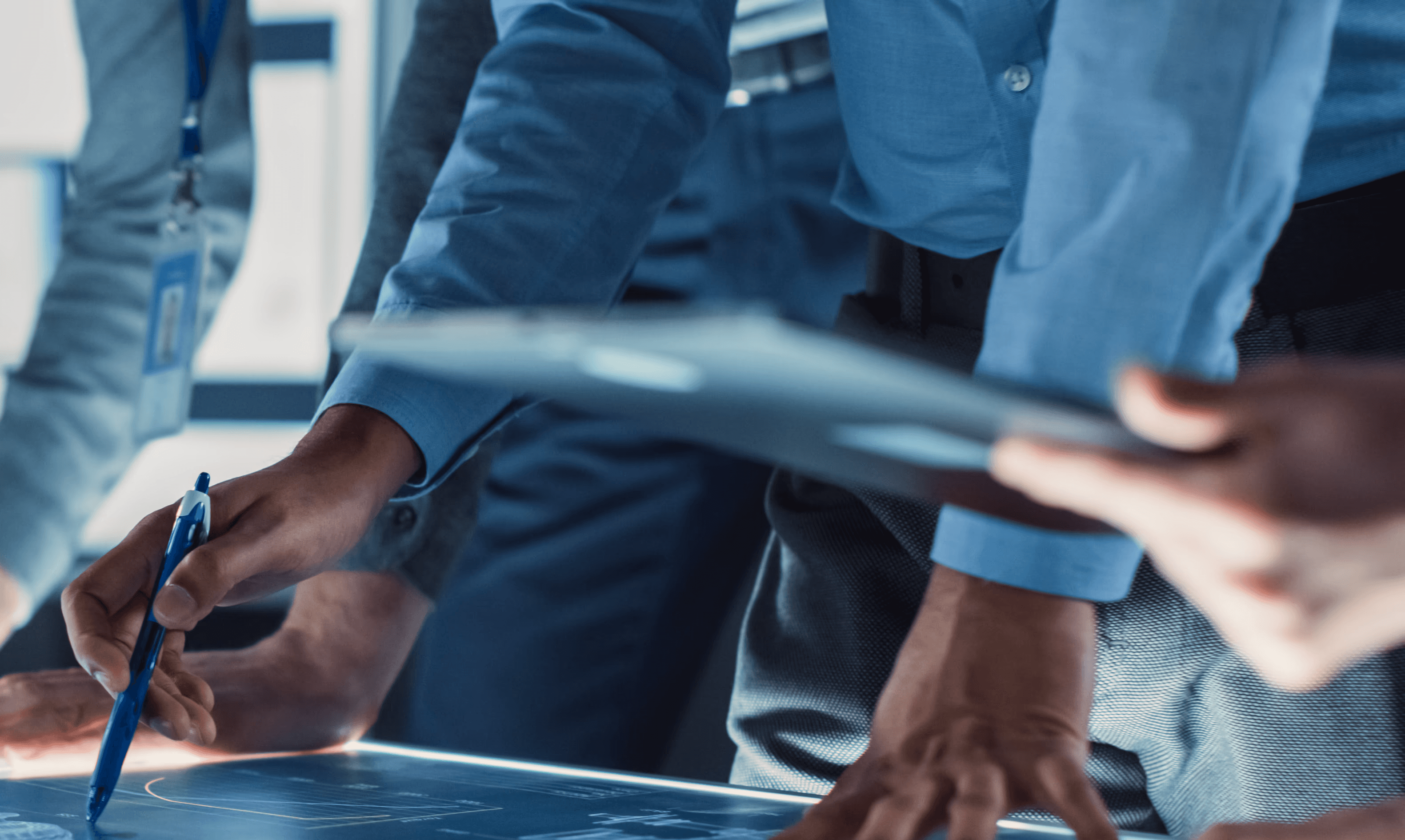A diverse team of professionals collaborating around an illuminated digital display table, reviewing data and plans in a modern work environment.