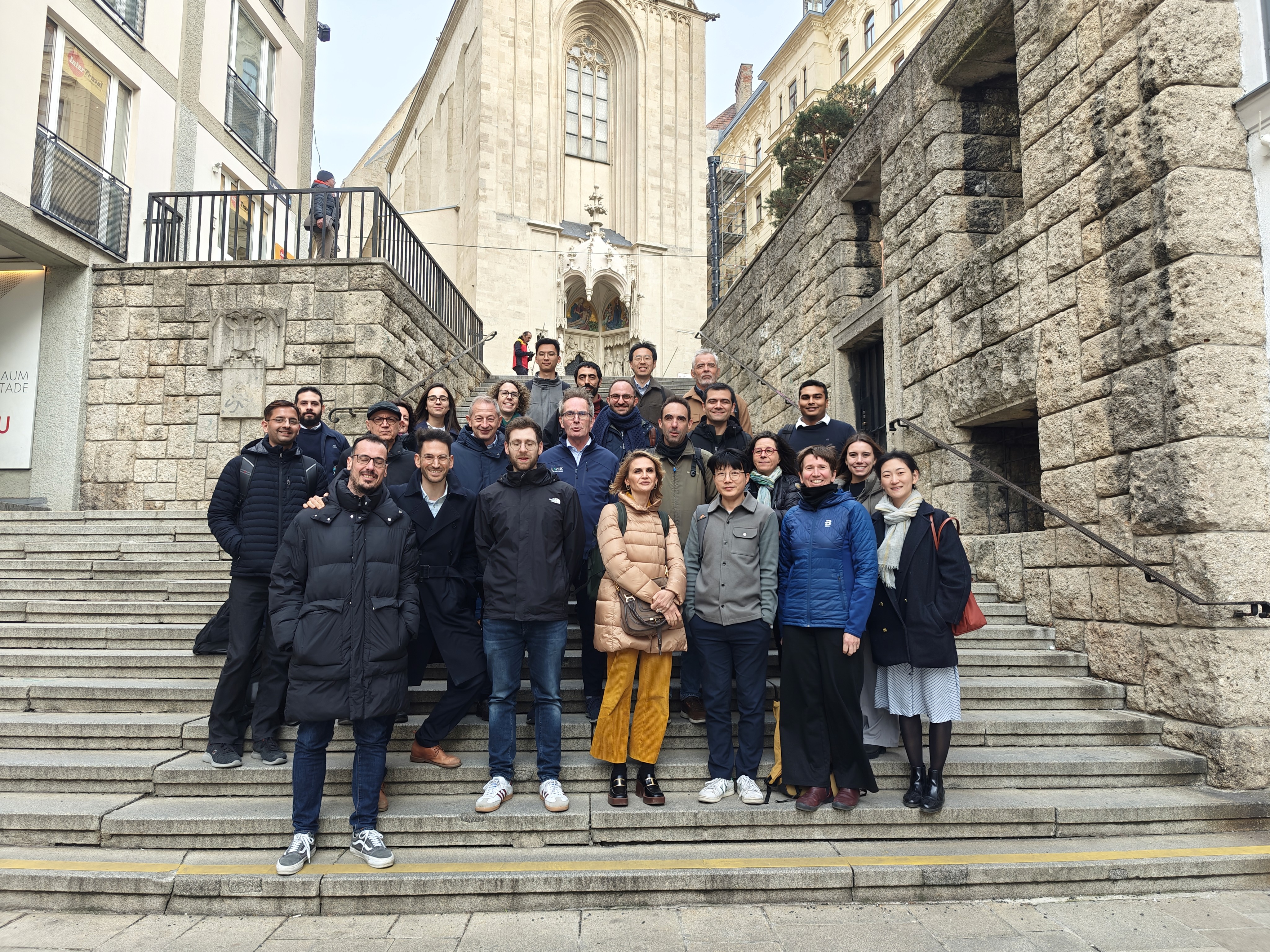 A large group of people poses for a photo on stone steps in front of an old church.