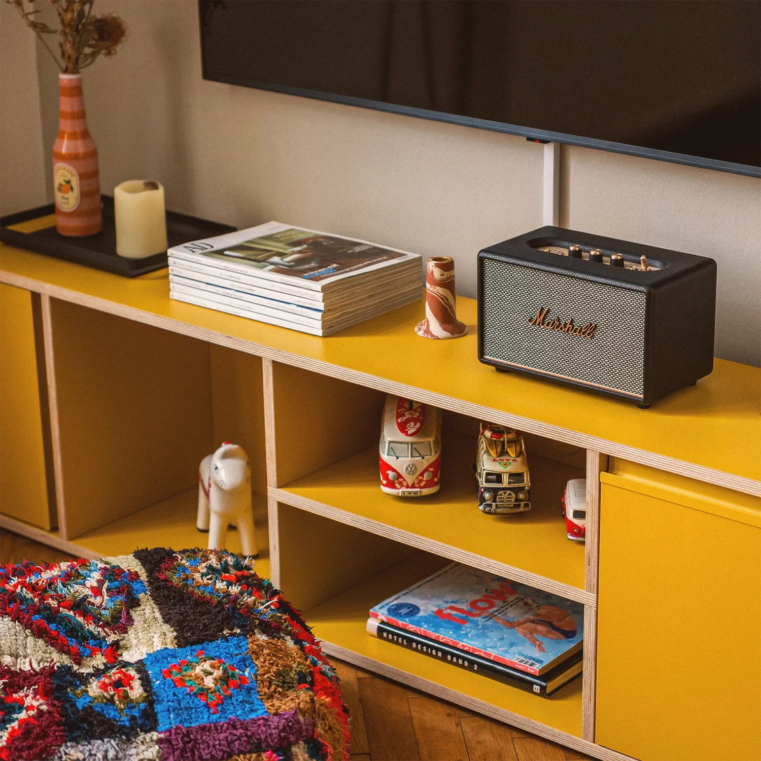 Boutique N°1 • yellow sideboard with a Marshall speaker, vintage toy cars and a colourful patchwork pouf